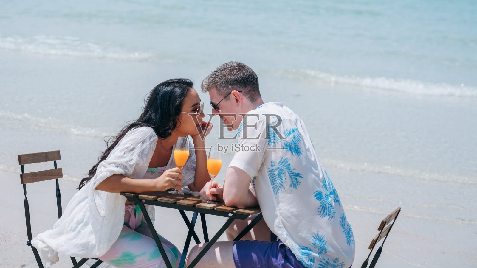 一对幸福相爱的年轻夫妇在热带海滩喝橙汁。在海边享受快乐和浪漫的情侣照片摄影图片