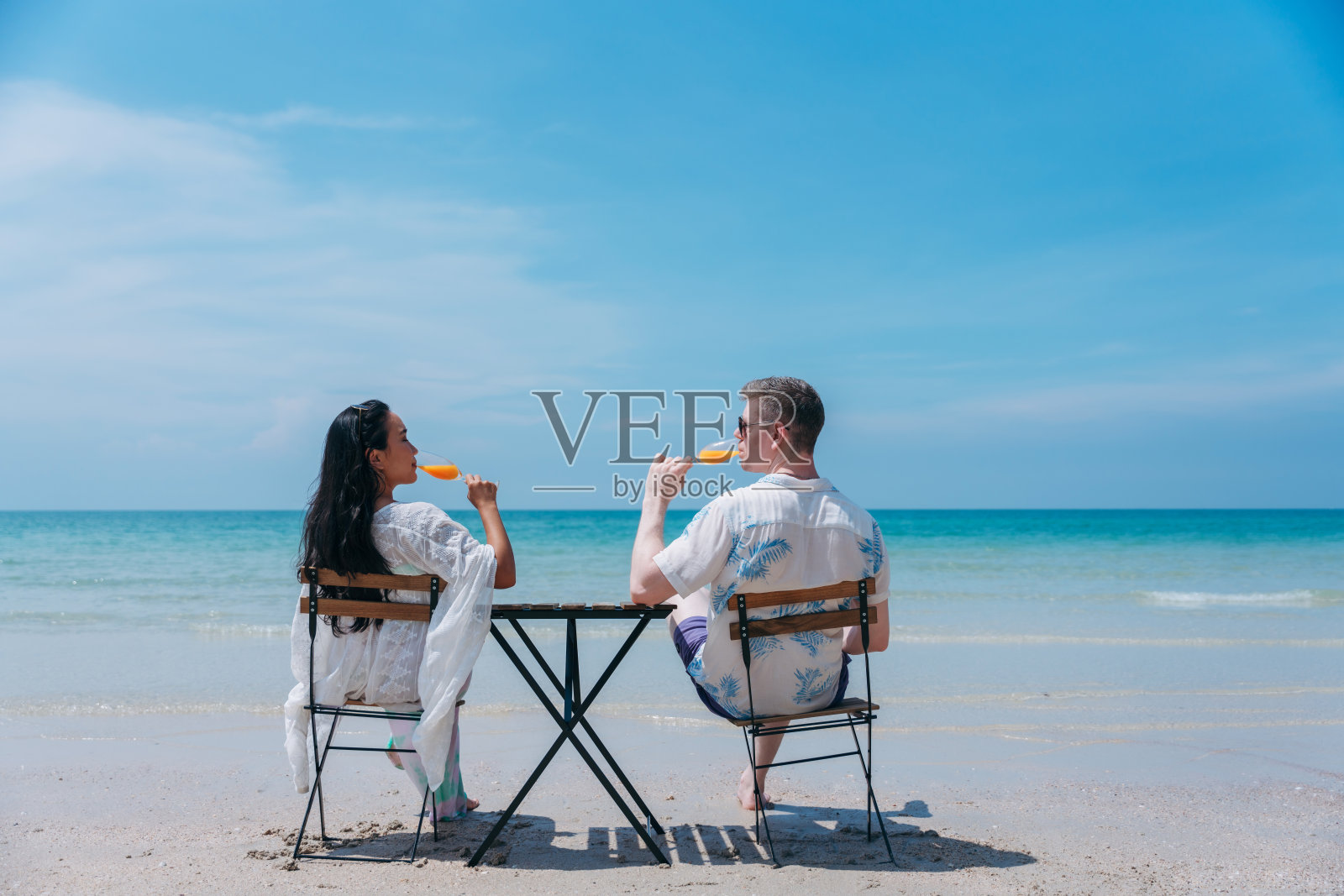 一对幸福相爱的年轻夫妇在热带海滩喝橙汁。在海边享受快乐和浪漫的情侣照片摄影图片