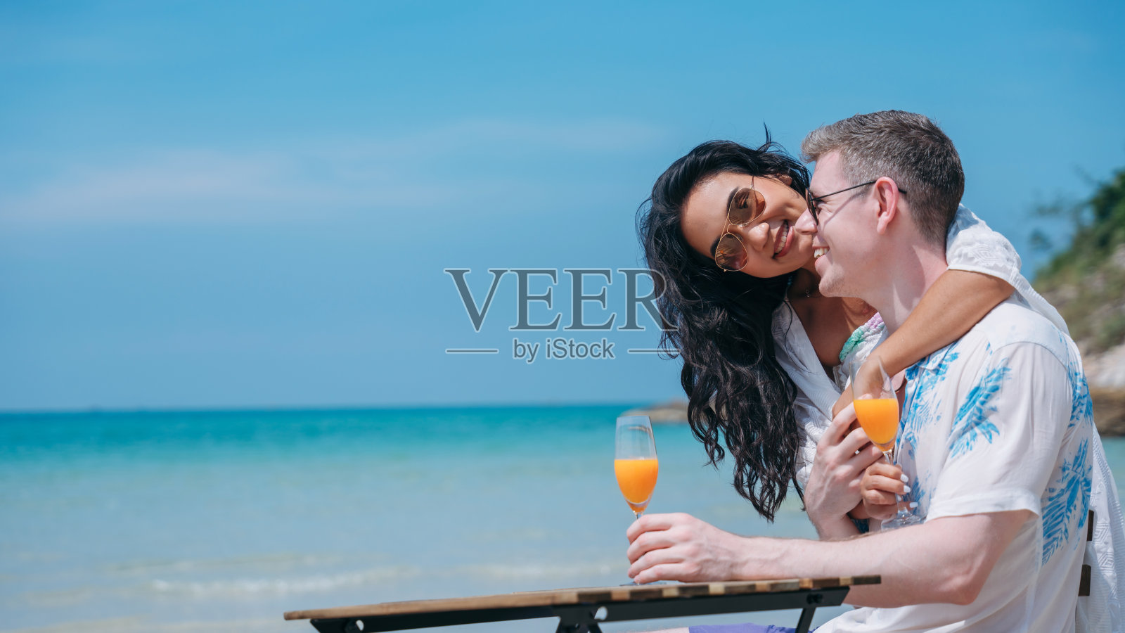 一对幸福相爱的年轻夫妇在热带海滩喝橙汁。在海边享受快乐和浪漫的情侣照片摄影图片