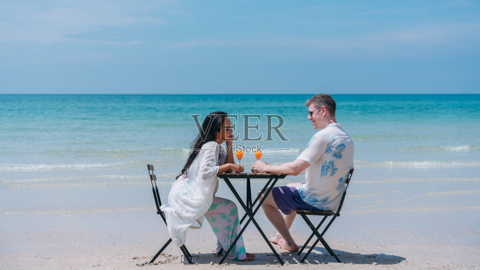 一对幸福相爱的年轻夫妇在热带海滩喝橙汁。在海边享受快乐和浪漫的情侣照片摄影图片