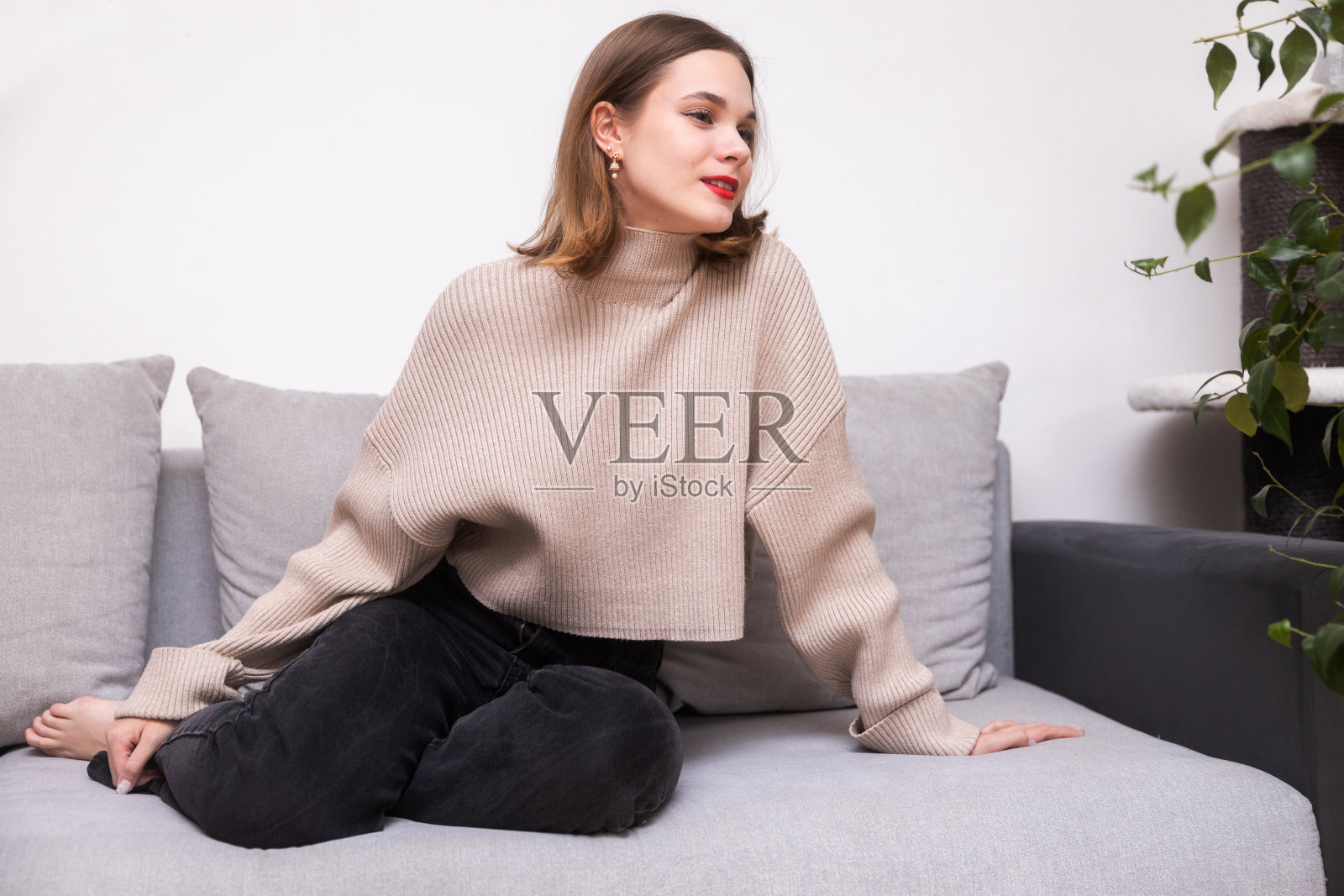 可爱的女孩穿着舒适温暖的毛衣坐在沙发上，看着别处照片摄影图片