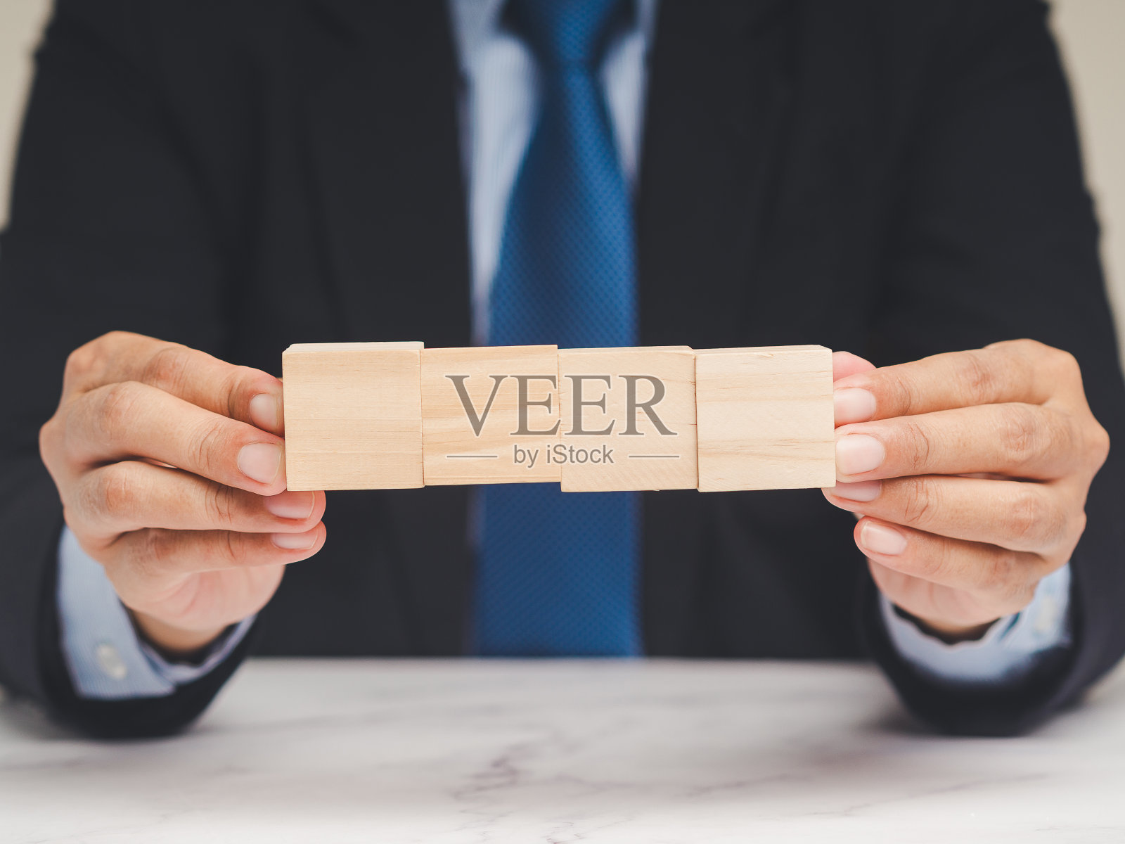 商人坐在桌旁，手里拿着四个空白的木立方体。照片摄影图片