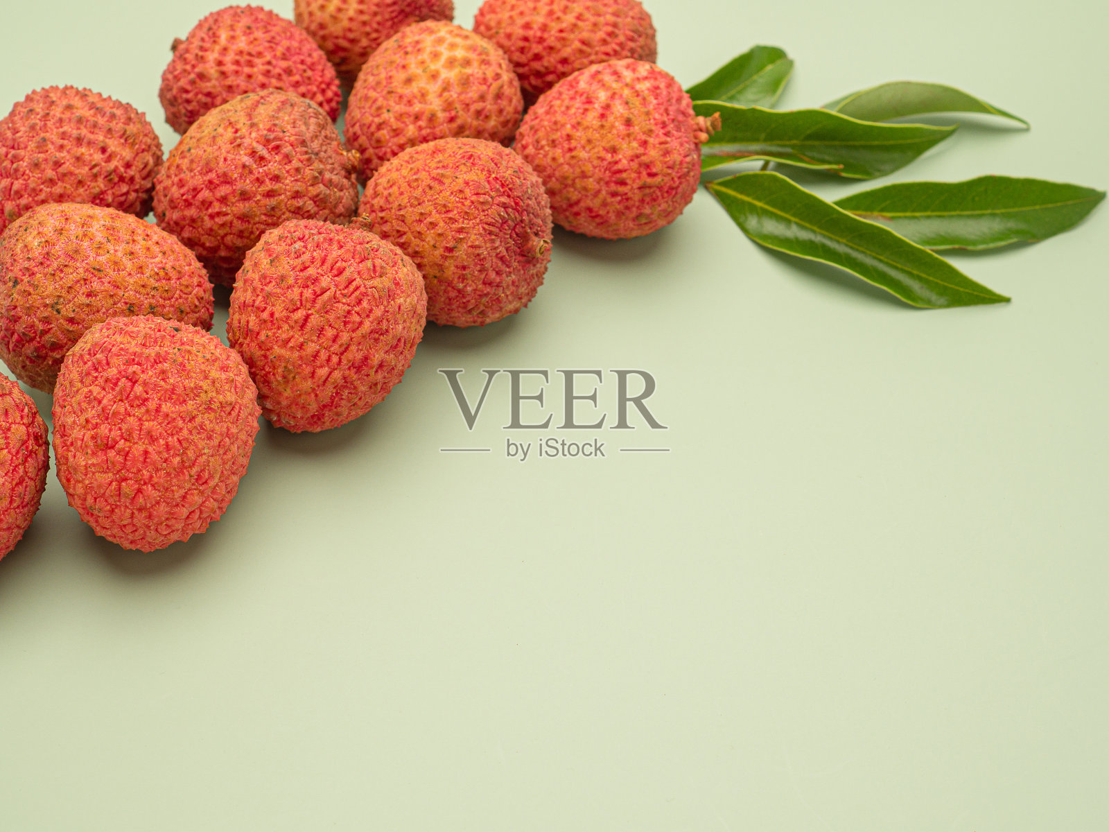 一堆新鲜成熟的荔枝，绿色的背景上点缀着绿叶。照片摄影图片