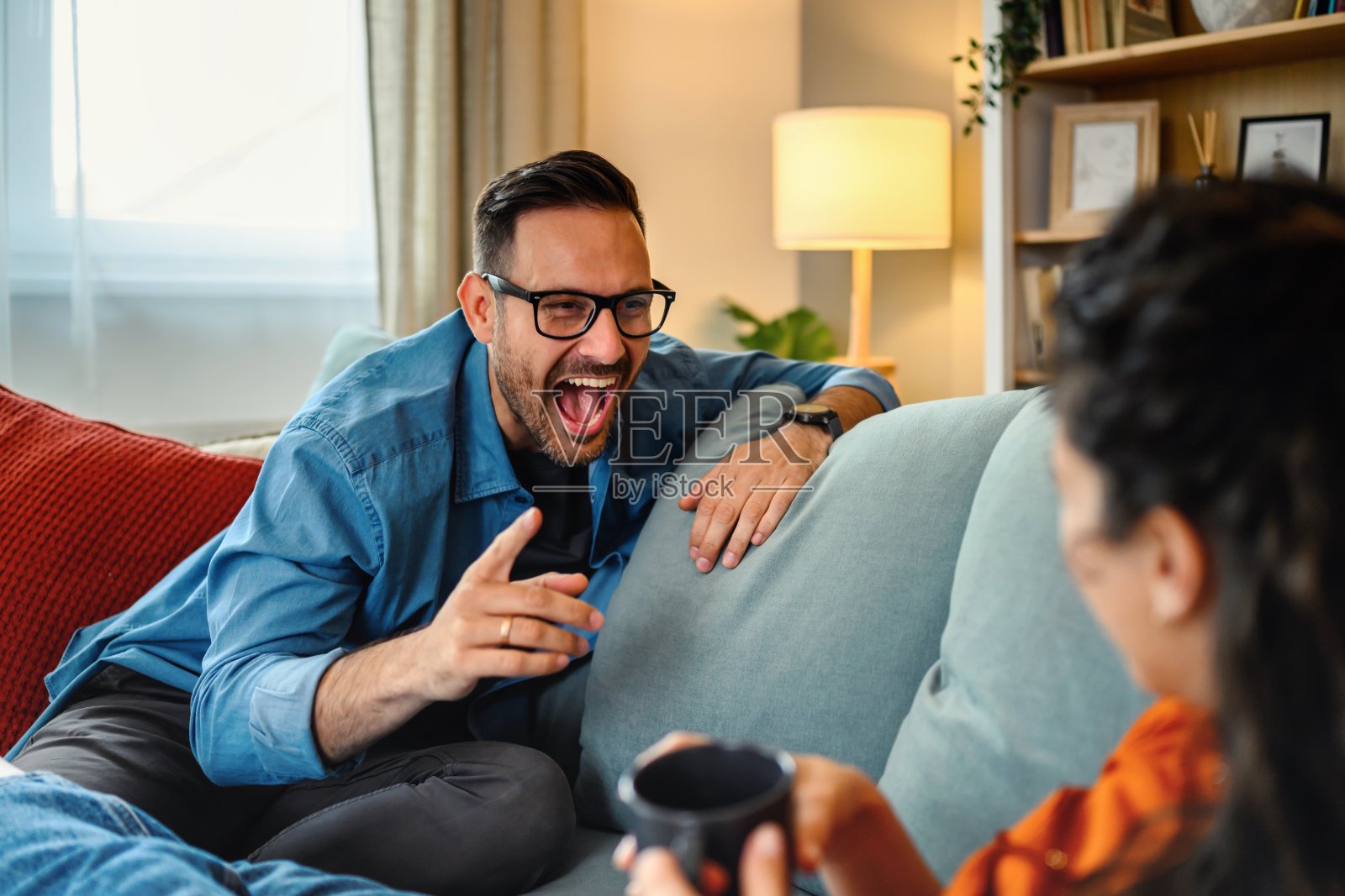 一对幸福的夫妇坐在客厅的沙发上大笑。照片摄影图片