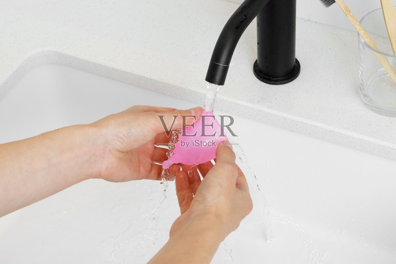 一位妇女在水槽上方的水流下洗手，手里拿着一个粉红色的月经杯。月经周期概念，月经期间可重复使用照片摄影图片