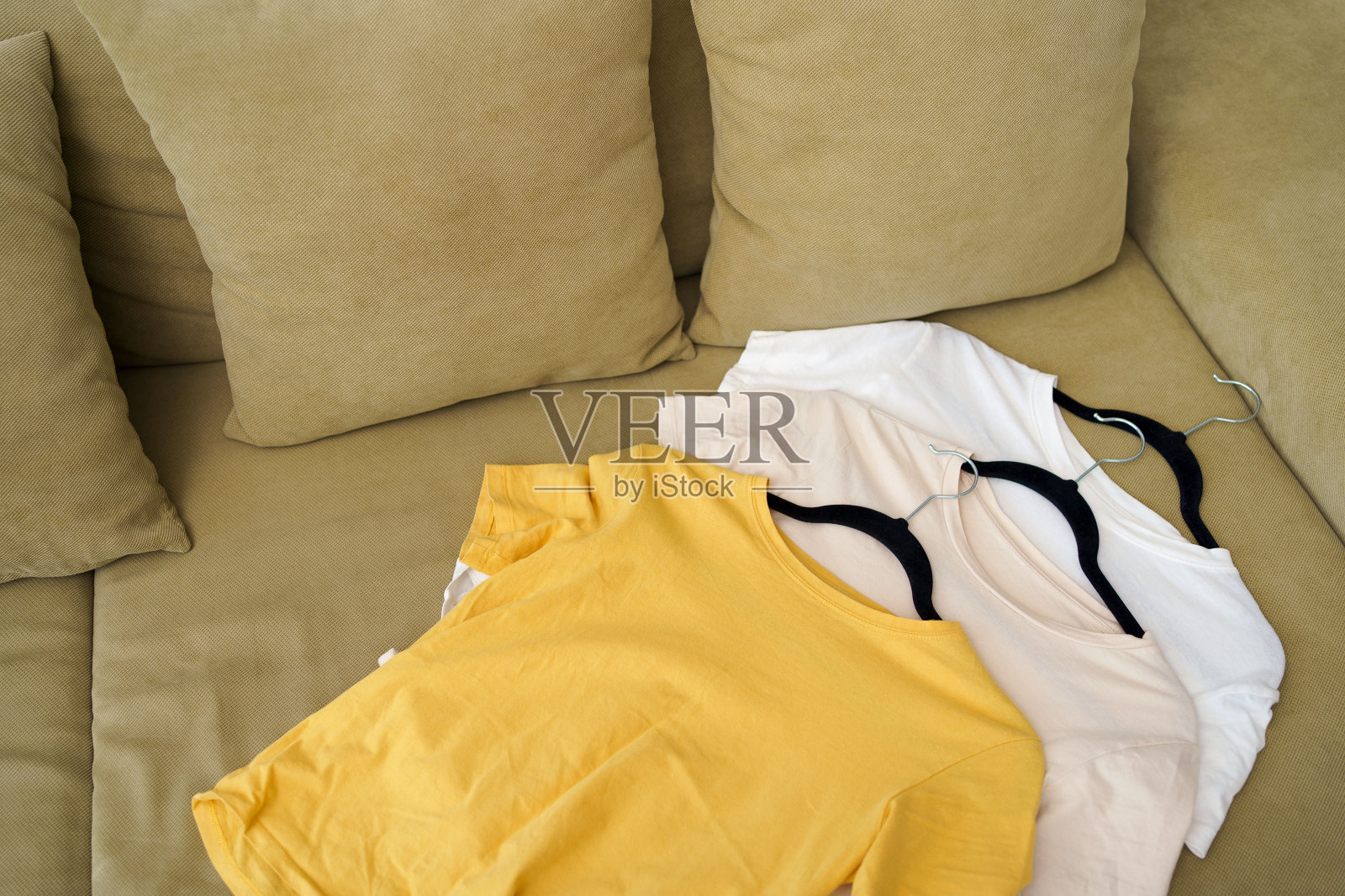 黄色、白色和米色的t恤放在衣架上，躺在沙发上。紧凑的概念存储在衣柜里，选择衣服和购买新衣服照片摄影图片