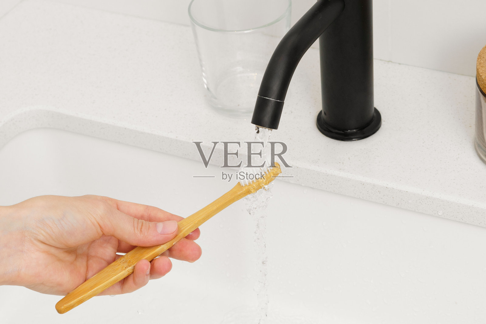 一个女人的手拿着一把天然的木制竹牙刷，在水槽上方的水流下。用牙膏清洁口腔的理念和可持续的生活方式照片摄影图片