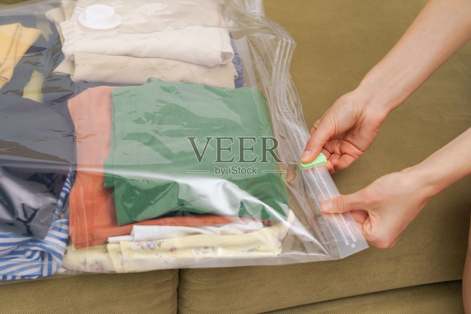 女人的手合上一个真空袋，里面装着衣服，便于紧凑的运输和储存在壁橱里。压缩包装，节省空间的理念照片摄影图片