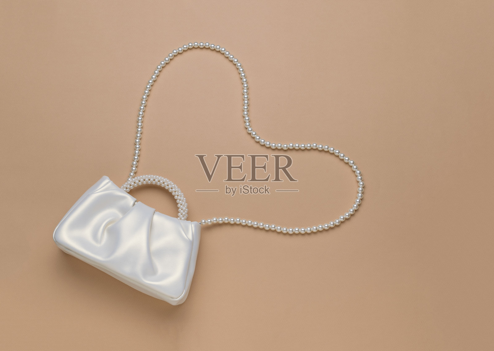 米色背景上有珍珠的白色袋子。照片摄影图片