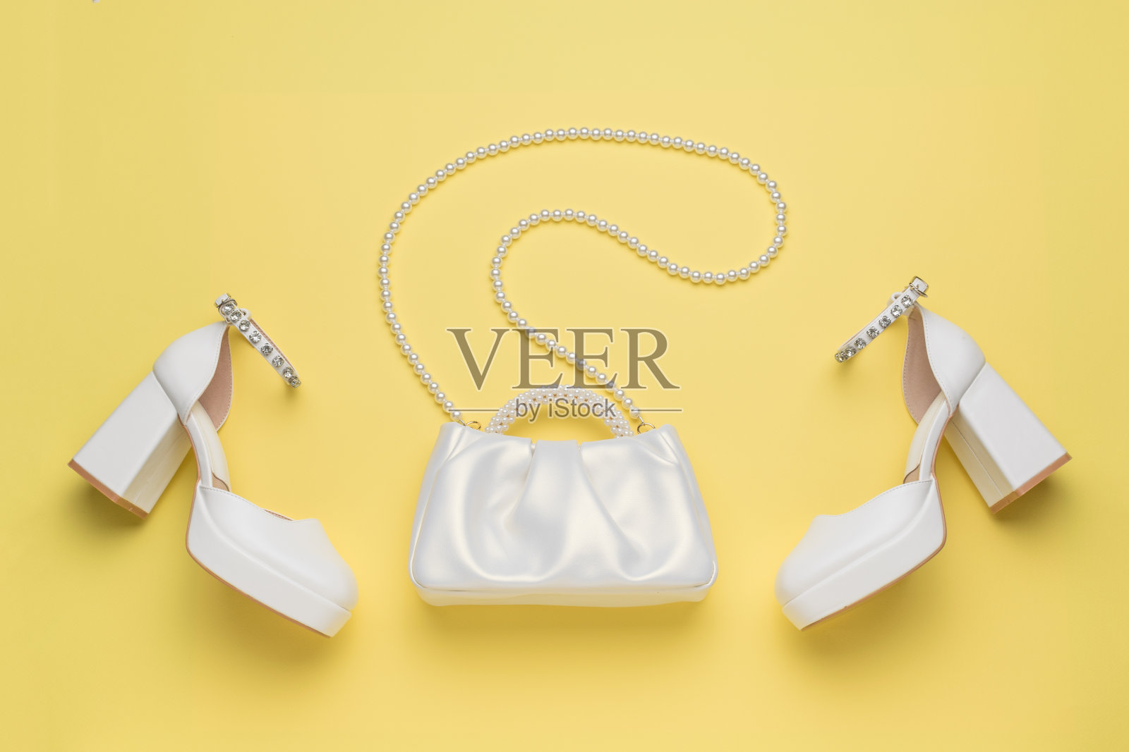 一双白色的女鞋和一个黄色背景的白色包包。照片摄影图片