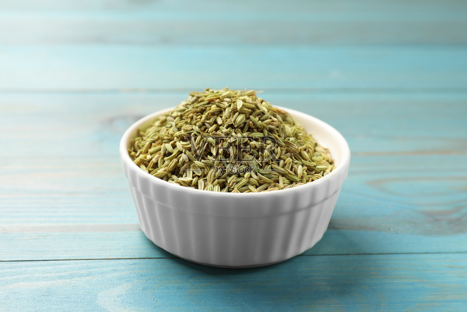 浅蓝色木桌上碗里的茴香籽，特写照片摄影图片