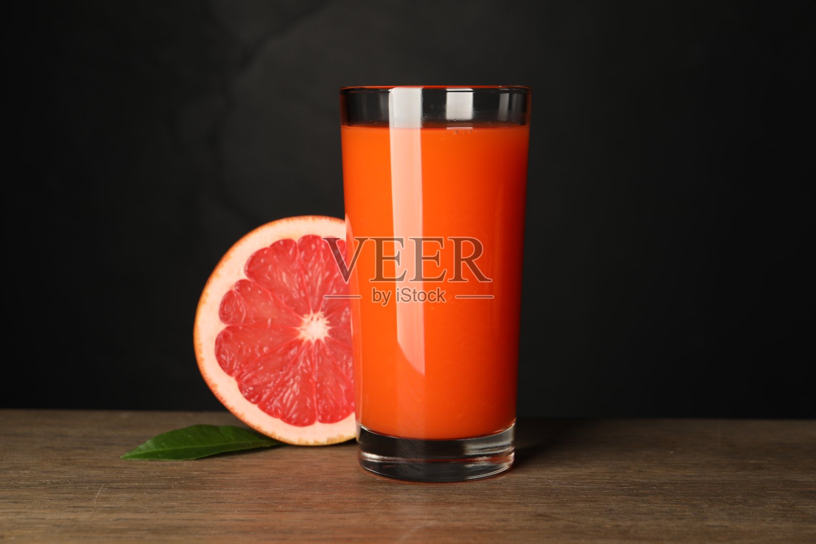 美味的葡萄柚汁在玻璃杯里，叶子和新鲜的水果在黑色背景的木桌上照片摄影图片
