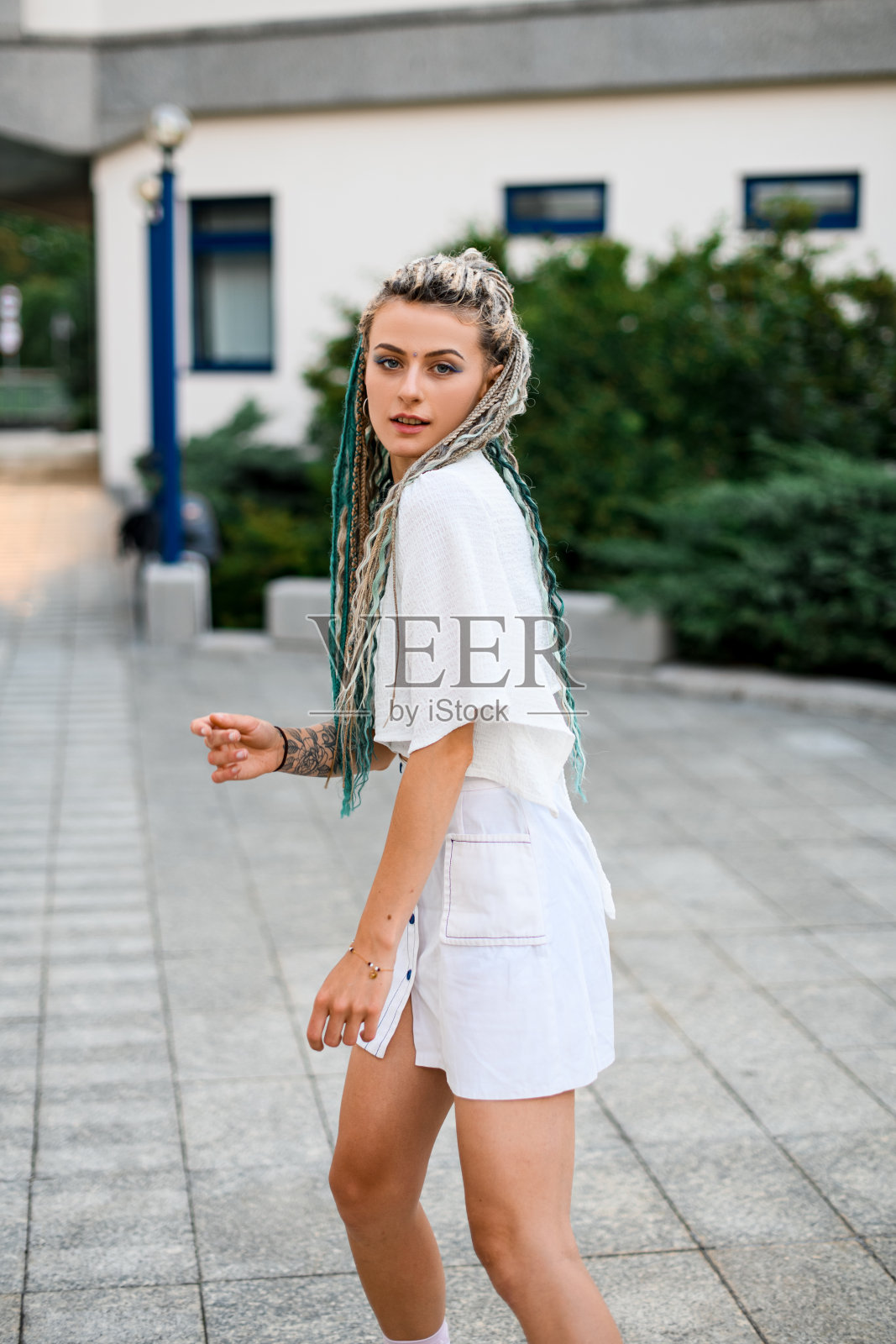 若有所思的金发女人穿着白色衣服，在模糊的城市街道背景下摆姿势照片摄影图片