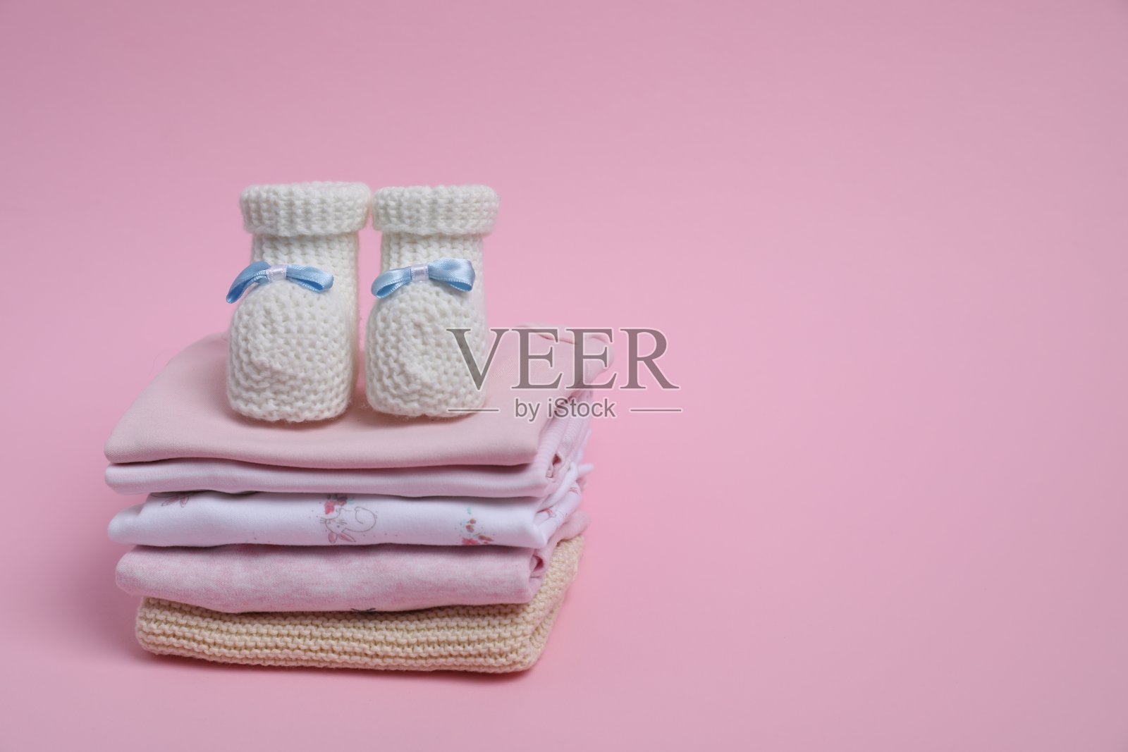 粉红色背景上一堆干净的婴儿衣服和小靴子。文本空间照片摄影图片