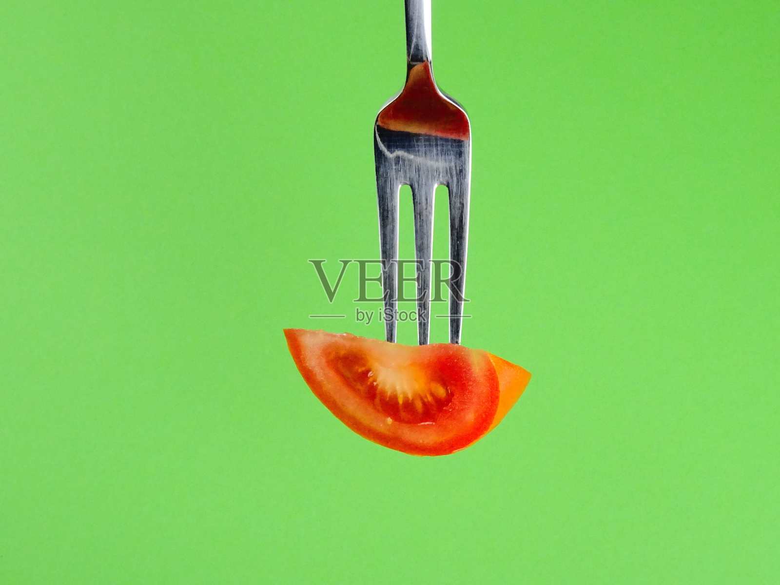 多汁的番茄片，用叉子夹在绿色背景上照片摄影图片