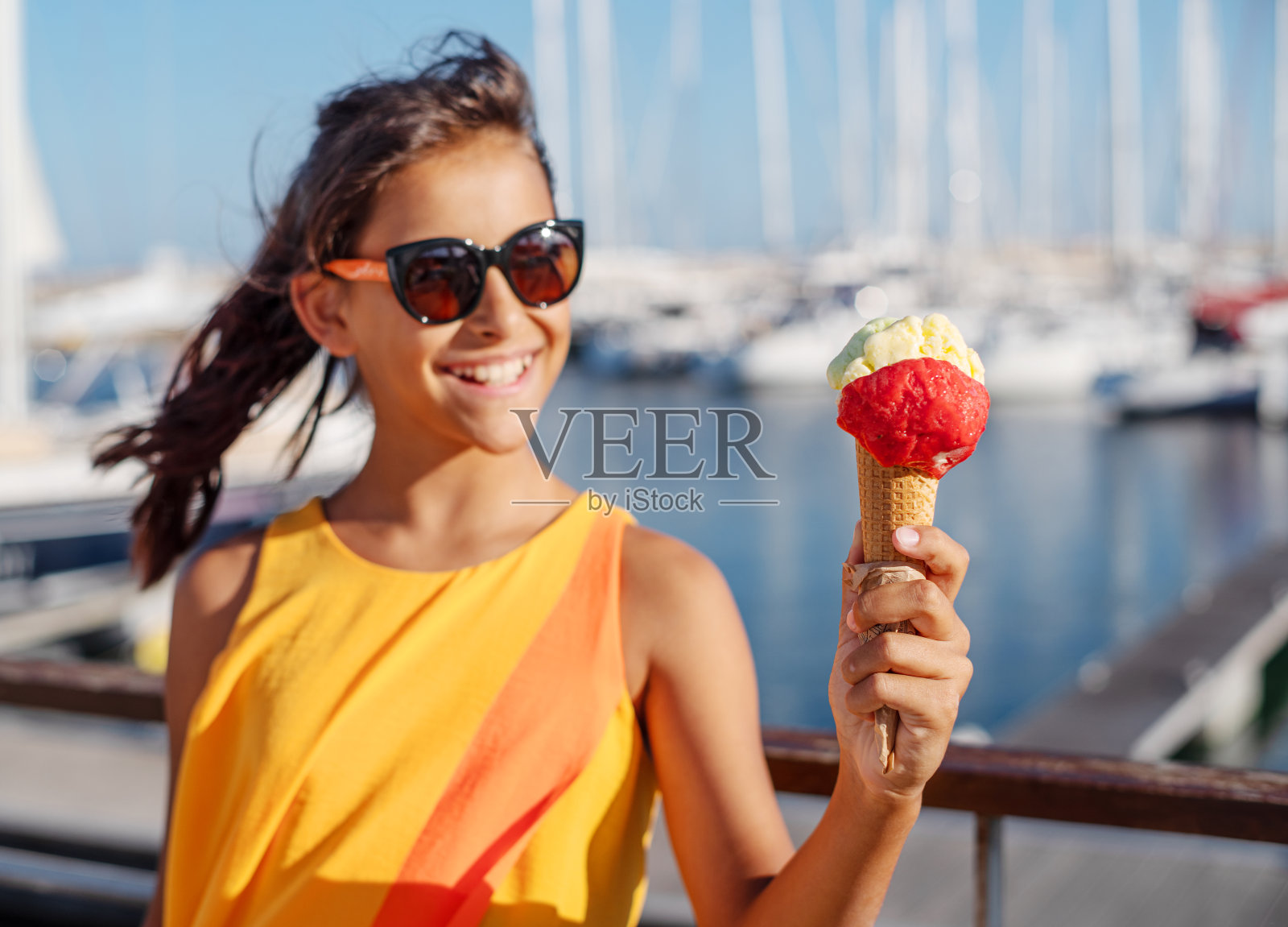 快乐，微笑的女孩拿着冰淇淋筒和五颜六色的冰淇淋球。背景是阳光明媚的海岸线。照片摄影图片