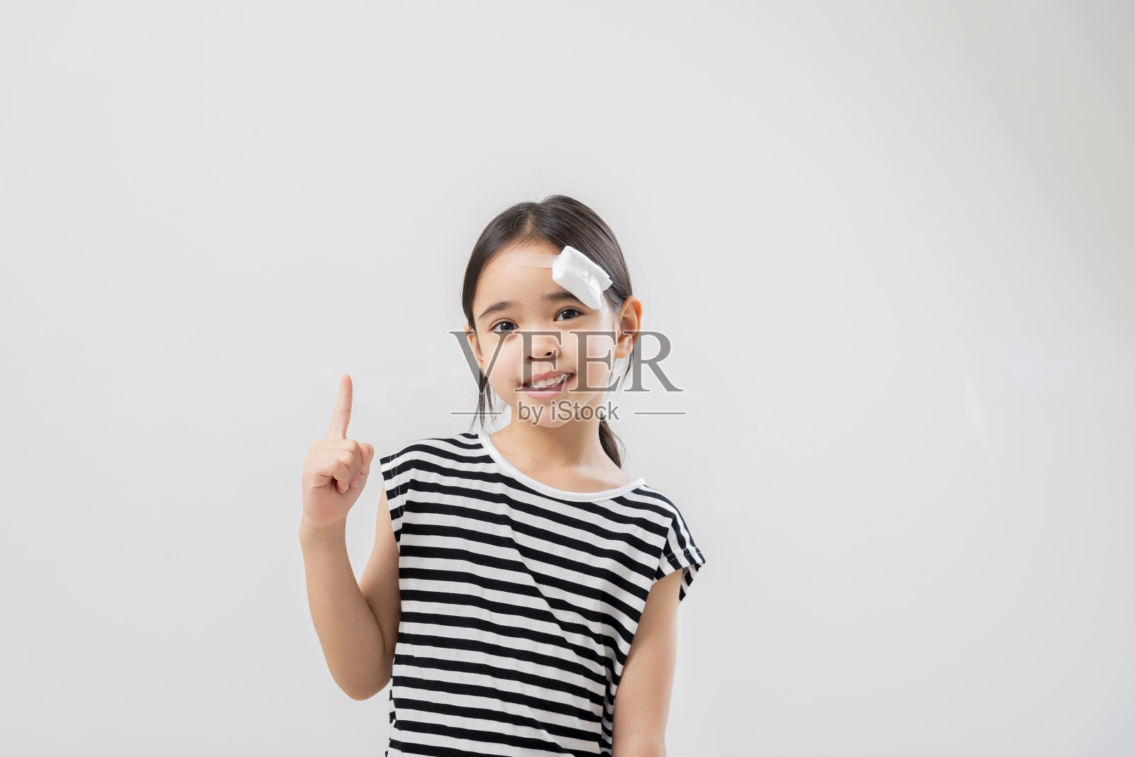 可爱的亚洲女孩站着，愉快地微笑，头上有一个绷带。照片摄影图片