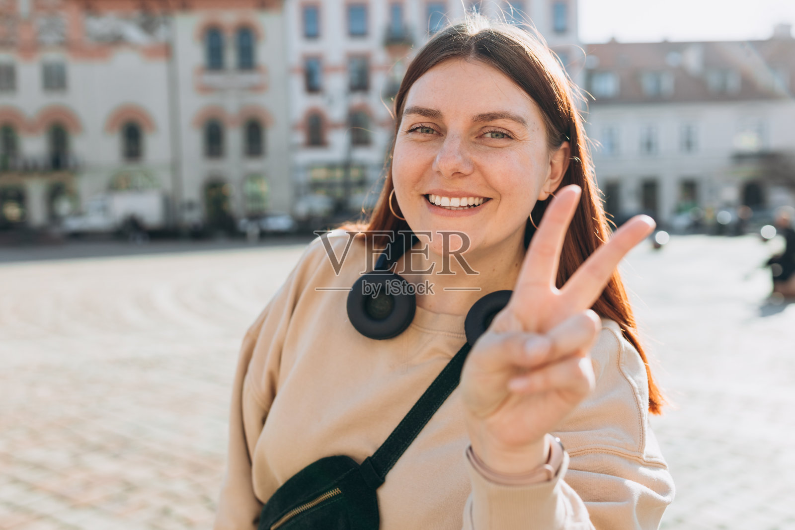 年轻的白人美女在春天的城市背景下做着和平手势。二号人物。积极生活方式概念照片摄影图片