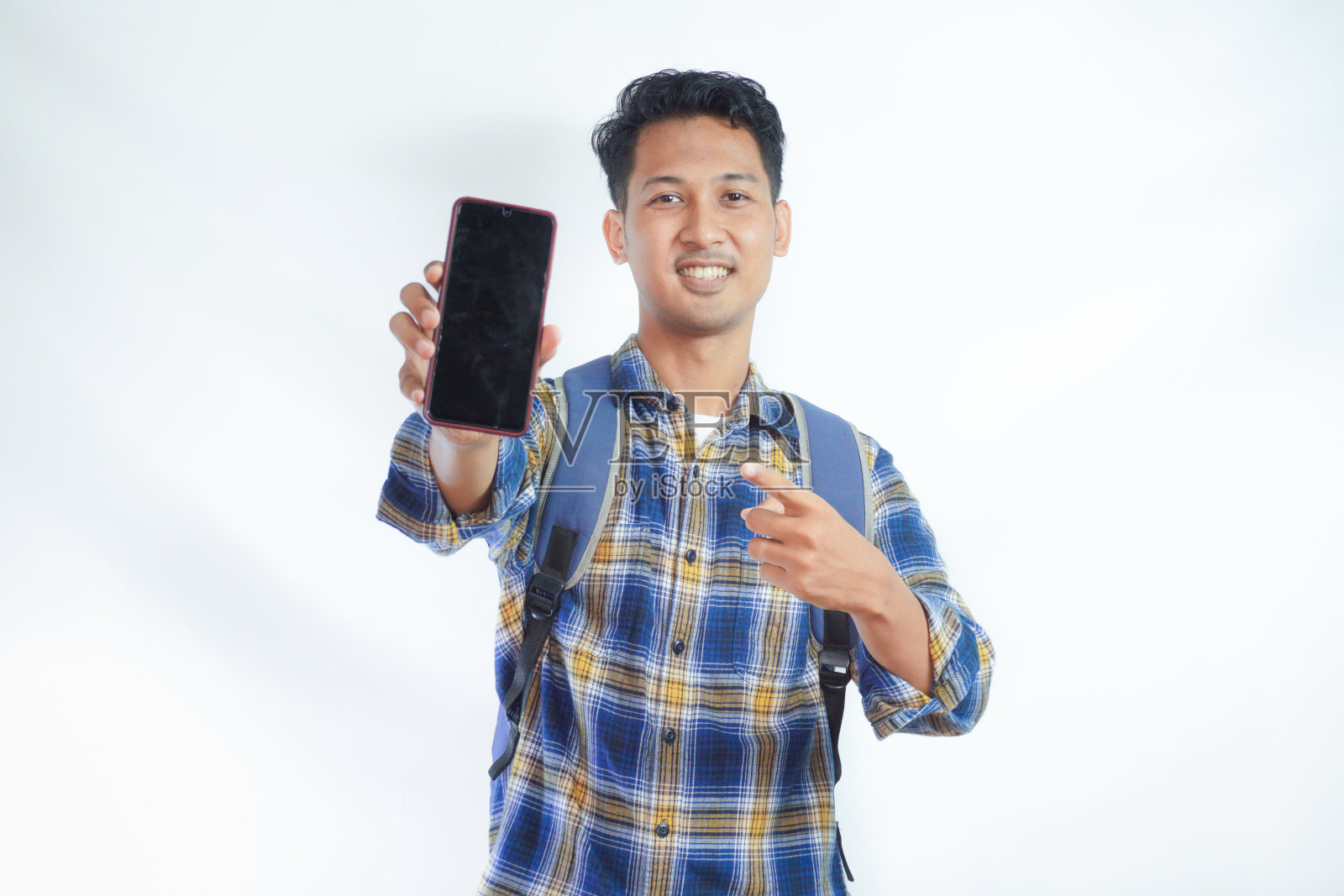 穿着休闲服，背着双肩包眼镜的开朗的年轻亚洲男学生，用手指着空白屏幕的手机，推荐孤立在白色背景上的应用程序。高中大学学院照片摄影图片