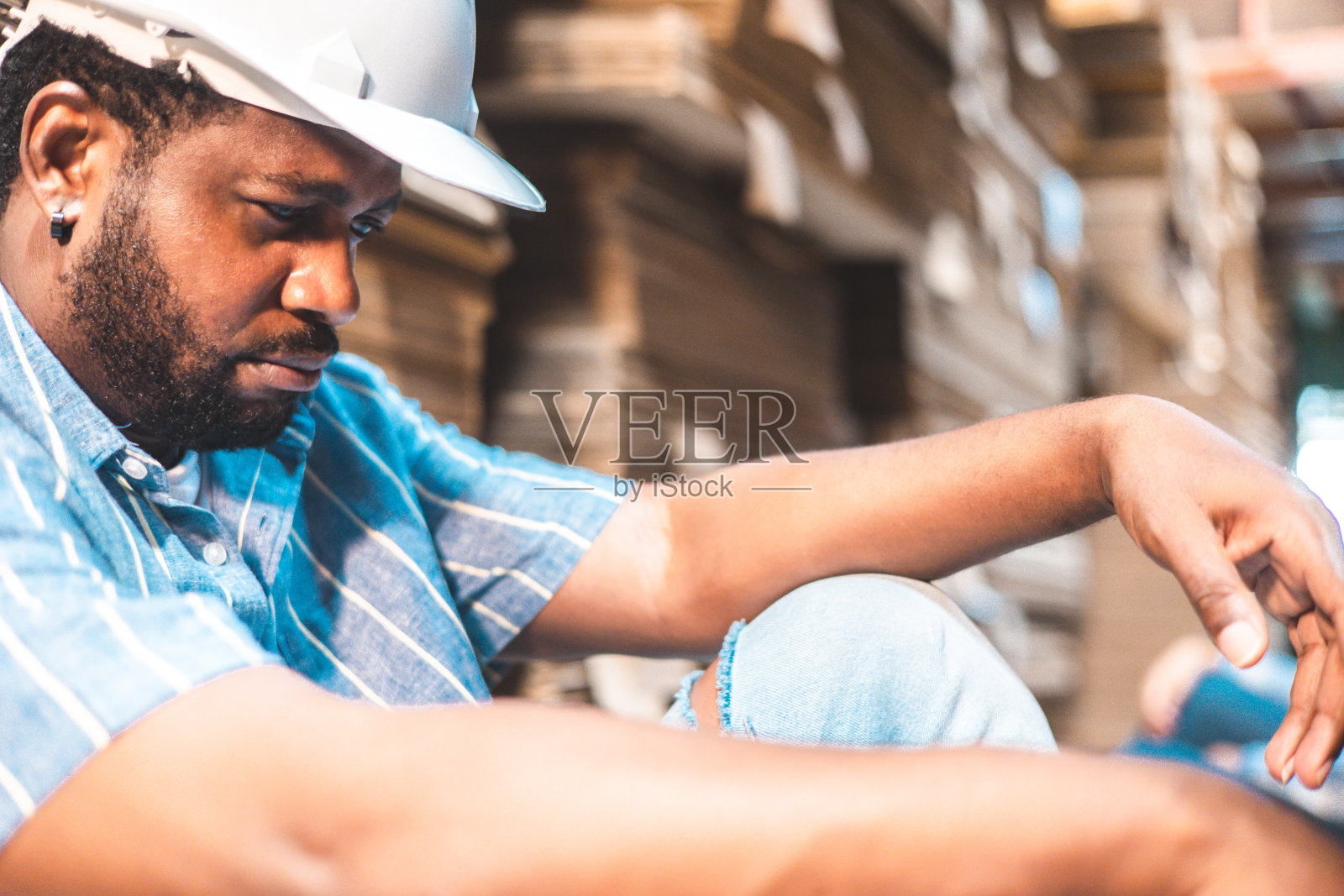 疲惫严肃的非洲男商人厂主坐在工厂里摆姿势。工程师或工人努力工作。失业感到压力。照片摄影图片