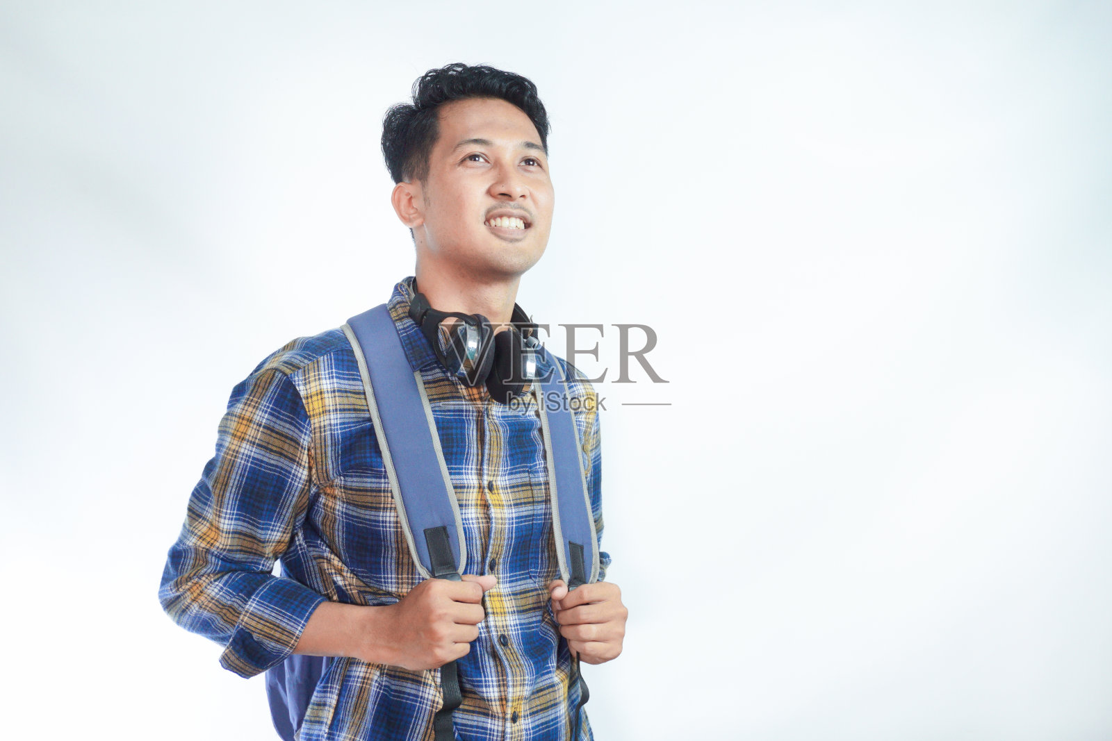 开朗的年轻亚洲学生穿着休闲装，背包望着空白的空间，新的招生广告孤立在白色背景上。高中大学学院的概念照片摄影图片