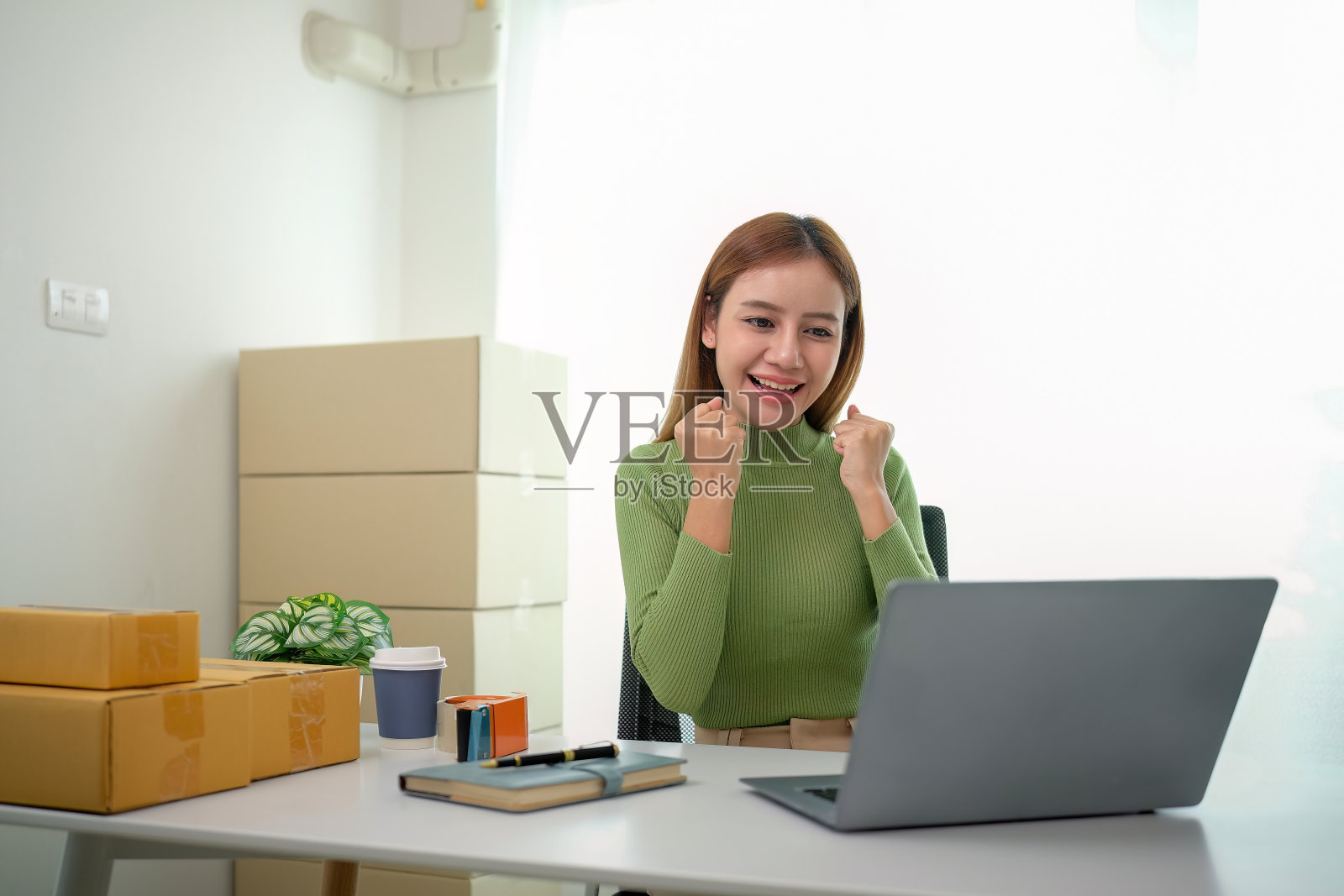 亚洲女性在销售增长方面取得了成功。快乐的女人用笔记本电脑在网上销售产品。美丽的年轻女性企业主关于网上业务照片摄影图片