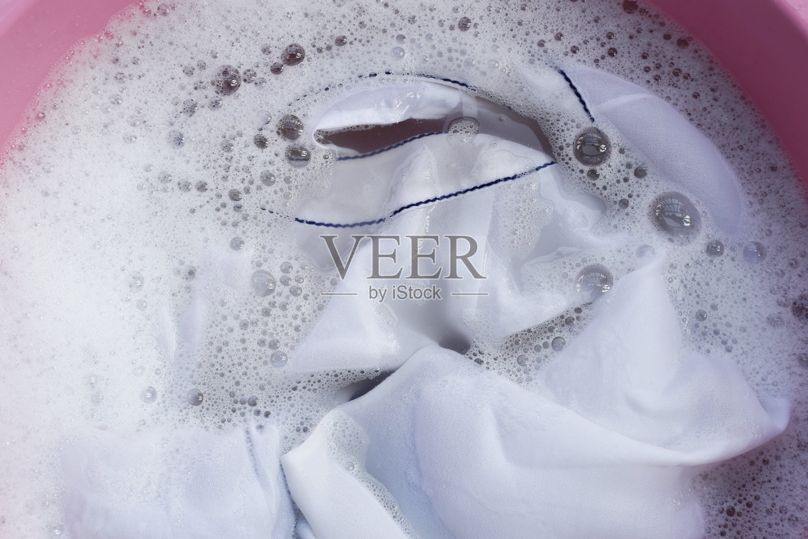 女士的衣服浸泡在水里溶解洗涤剂，产生白色的泡沫。衣服的概念照片摄影图片