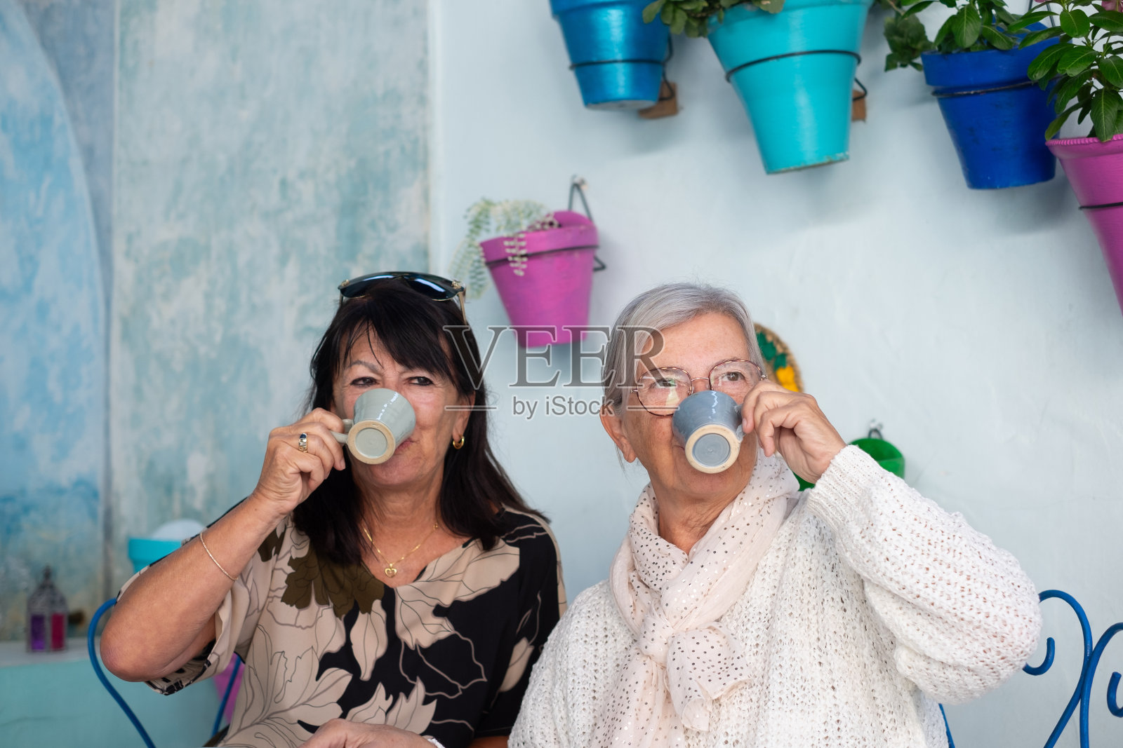 在西班牙科尔多瓦，一对老年妇女坐在鲜花盛开的庭院里的咖啡桌旁，喝着浓咖啡，享受着愉快的时光照片摄影图片