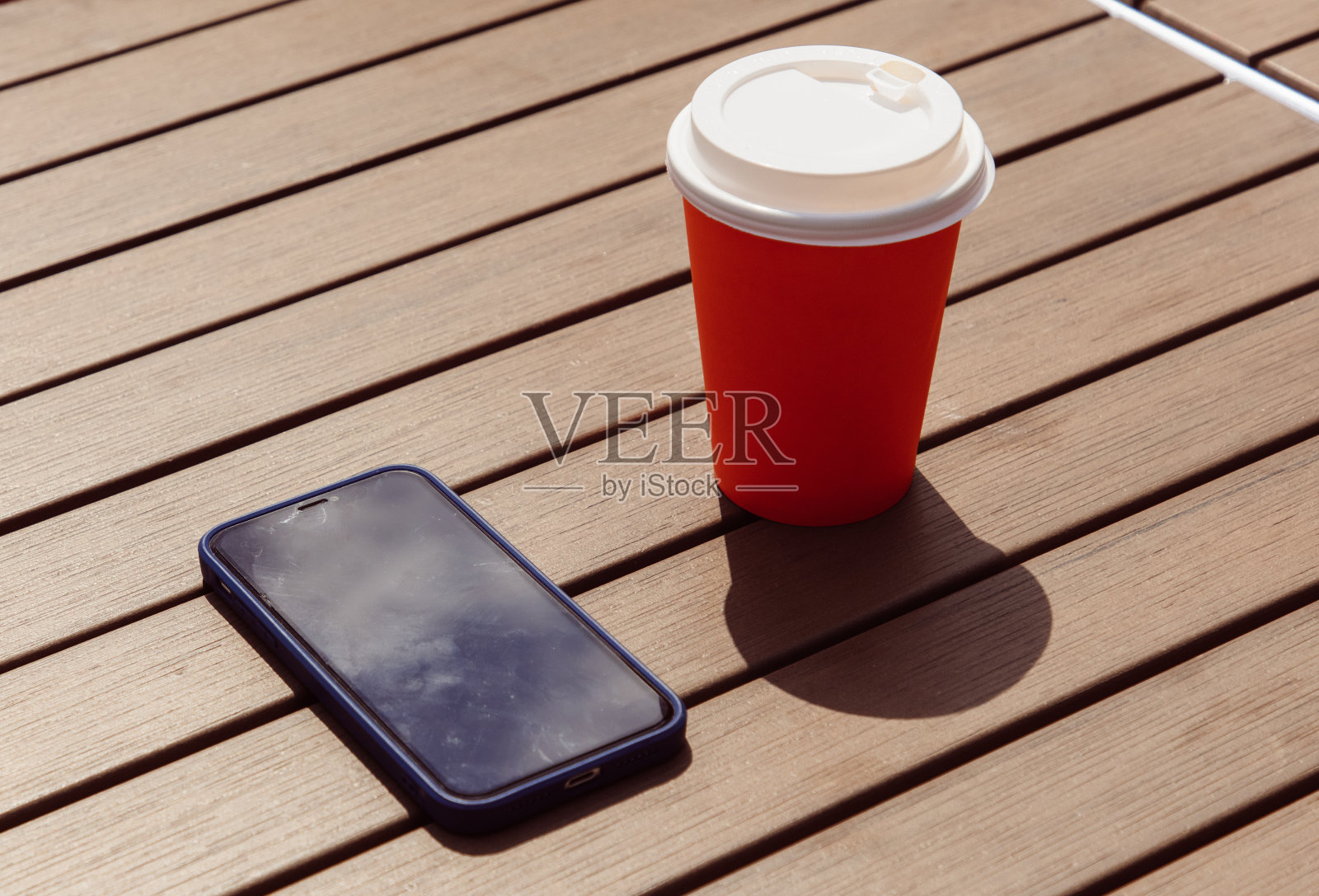 木桌上放着橙色的玻璃杯和电话。照片摄影图片