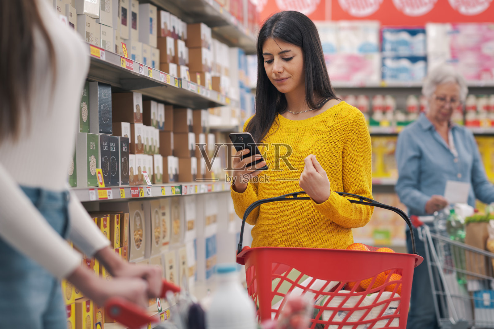 一个女人一边用智能手机一边在杂货店购物照片摄影图片