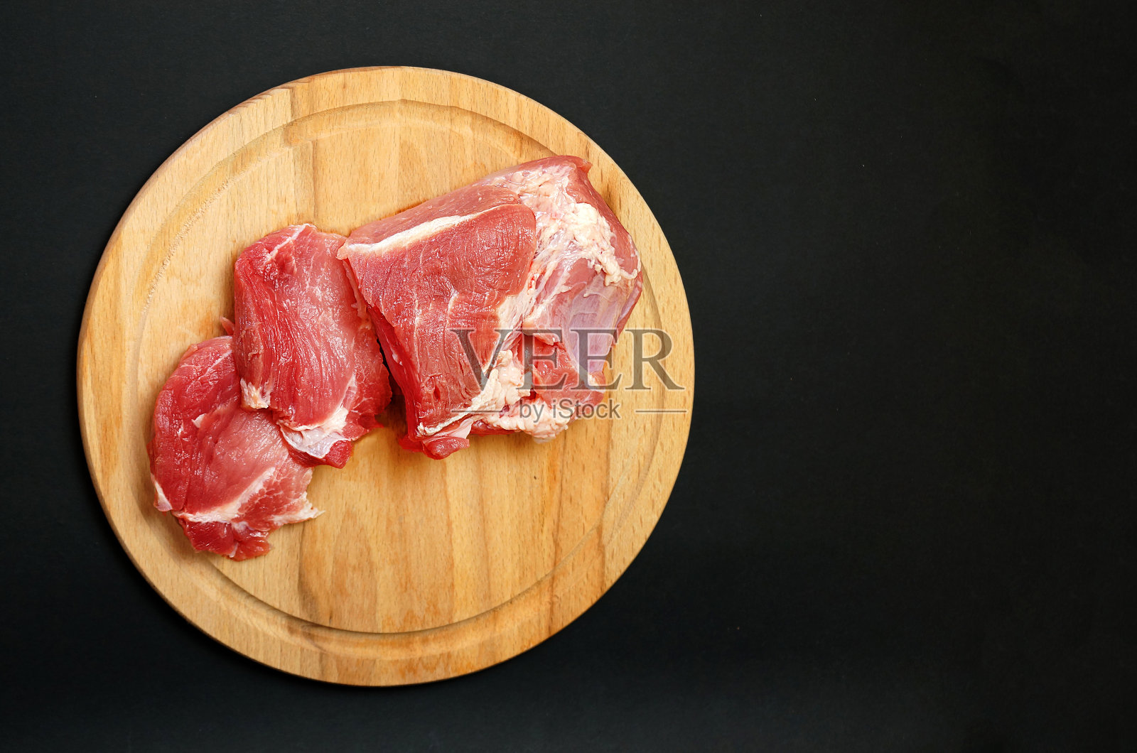 新鲜的猪肉片放在黑色背景的圆形木制砧板上，复制空间照片摄影图片