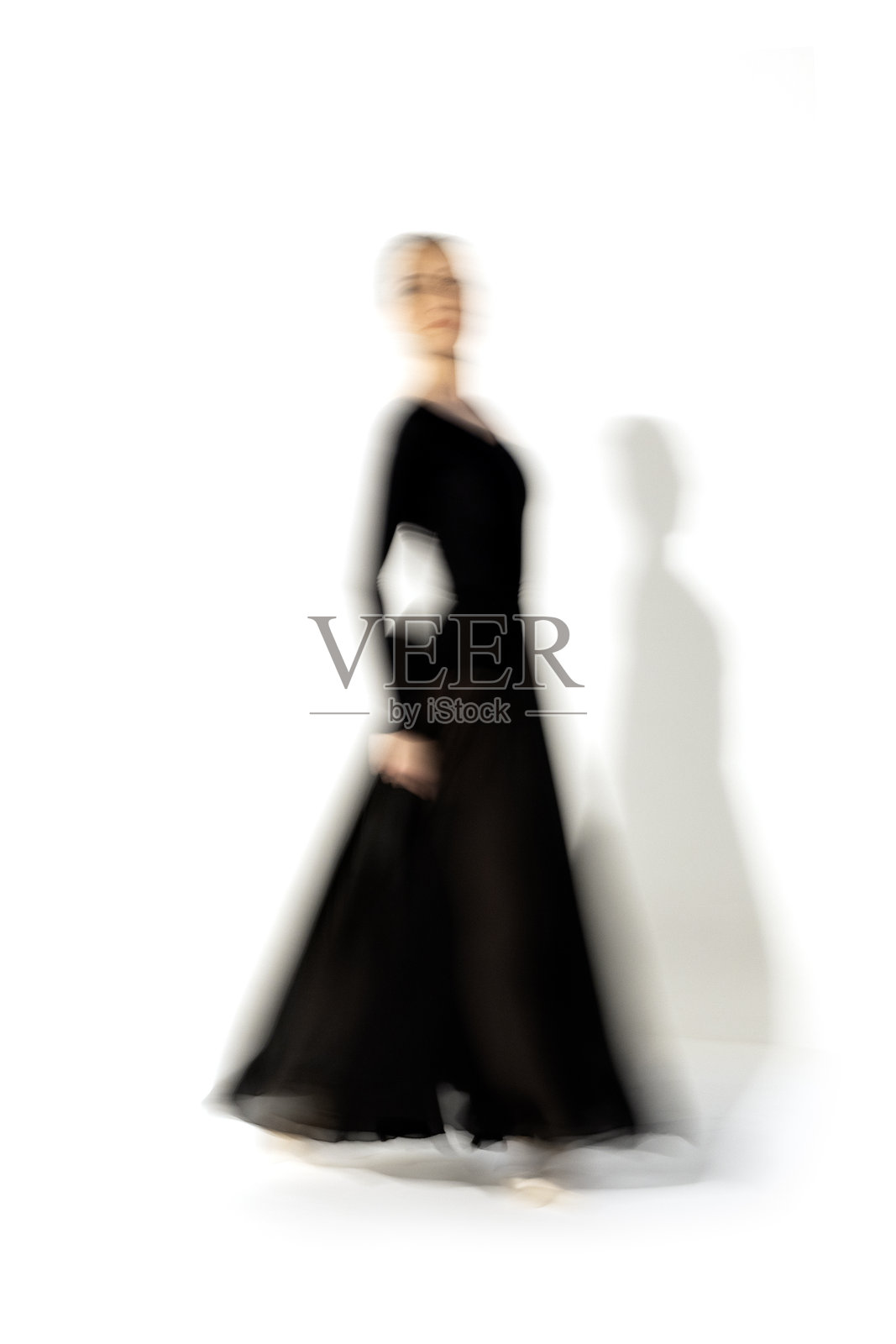 穿着黑色裙子的年轻芭蕾舞女演员在舞蹈室的灯光下跳舞。长时间的曝光。白色背景照片摄影图片