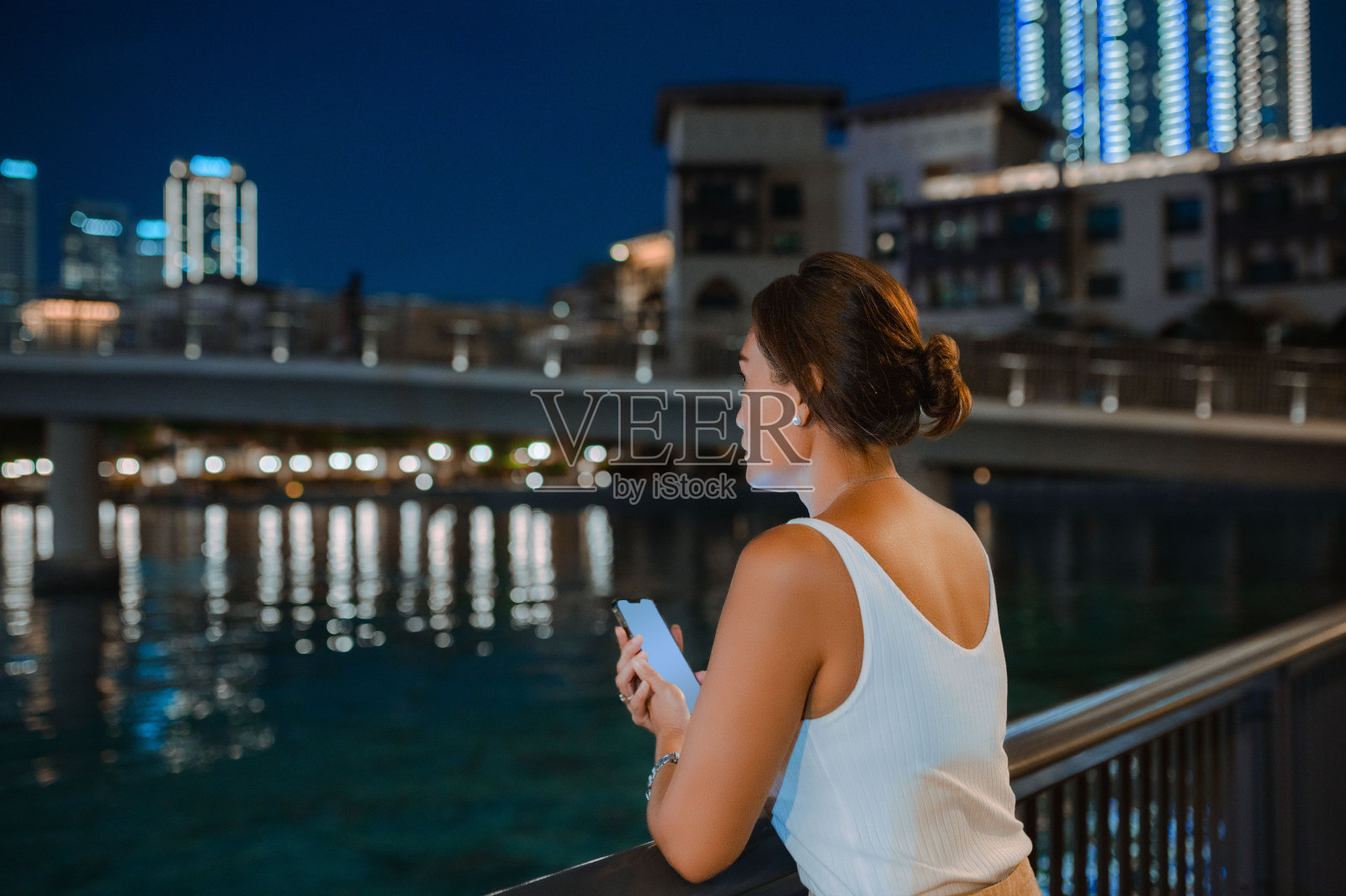 夜晚河边栏杆旁拿手机沉思女人背影照片摄影图片