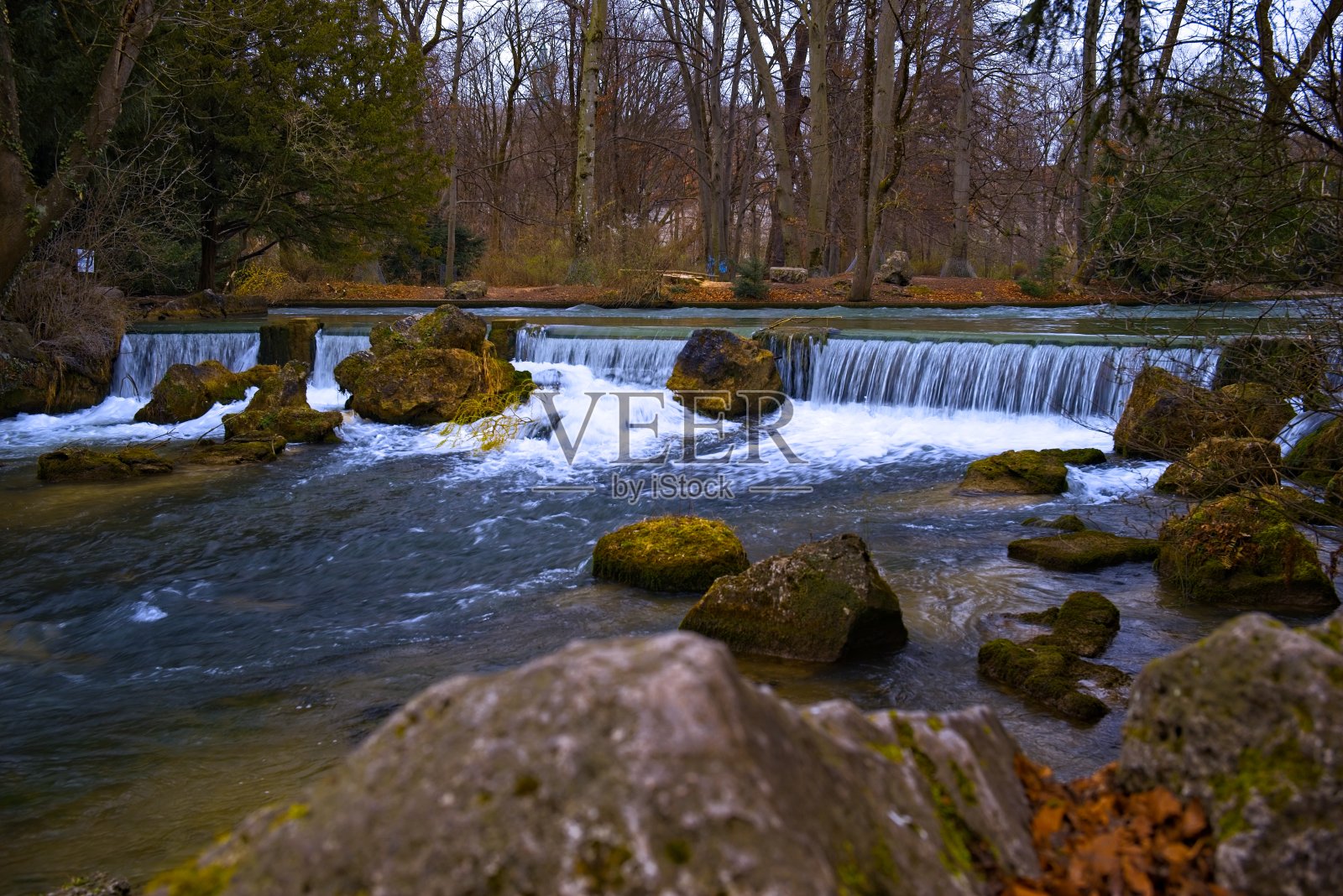 宁静的河流，瀑布倾泻而下，翠绿的岩石被秋天的森林包围。照片摄影图片