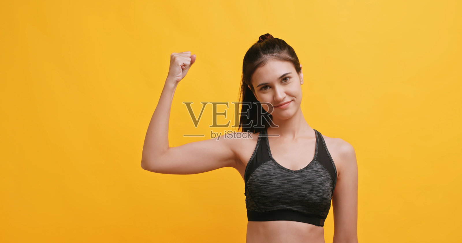 年轻的女运动员显示出体力。孤立在黄色背景的工作室。照片摄影图片