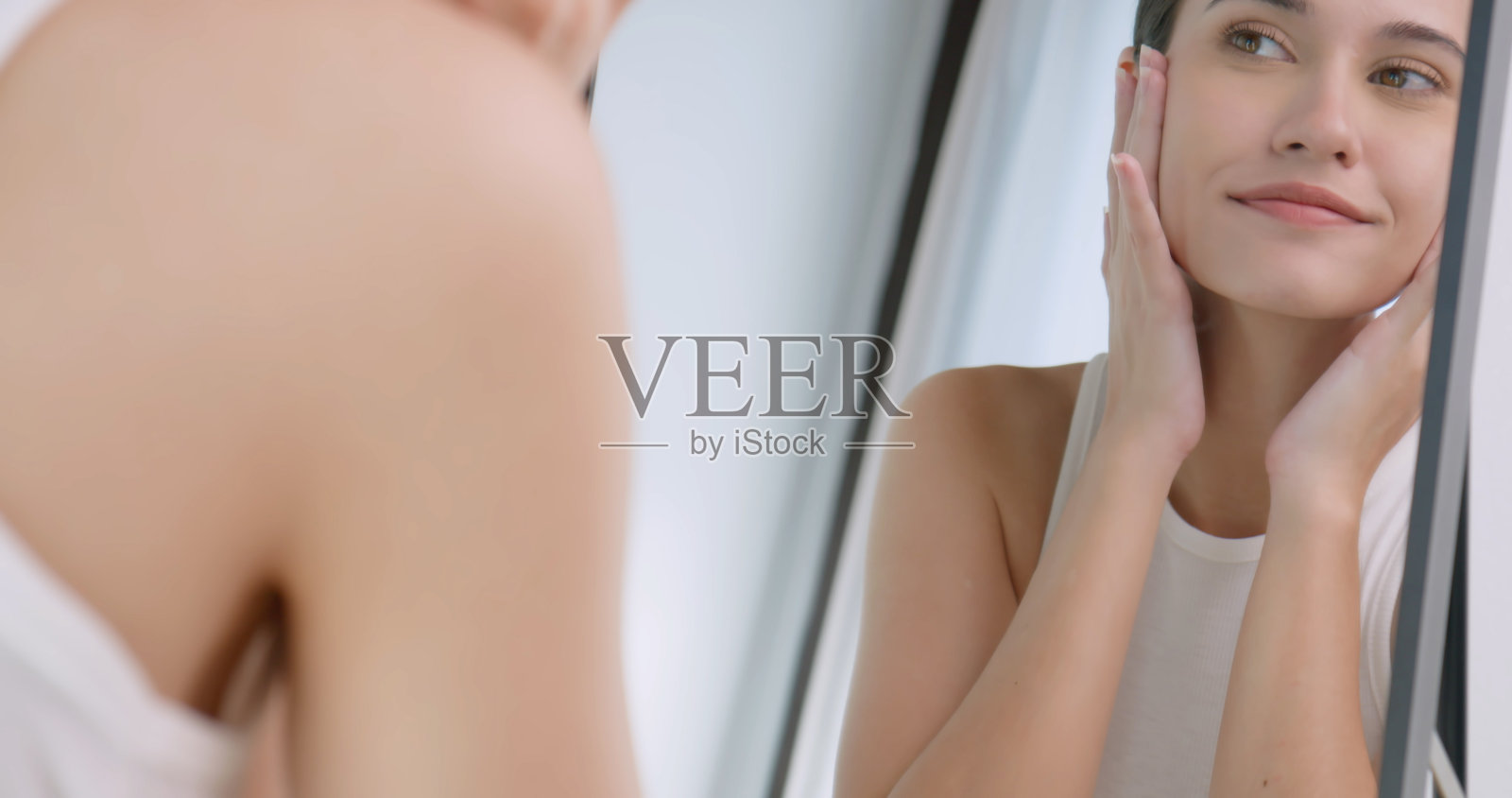 年轻女子站在镜子前，对自己的脸感到自信和自豪。照片摄影图片