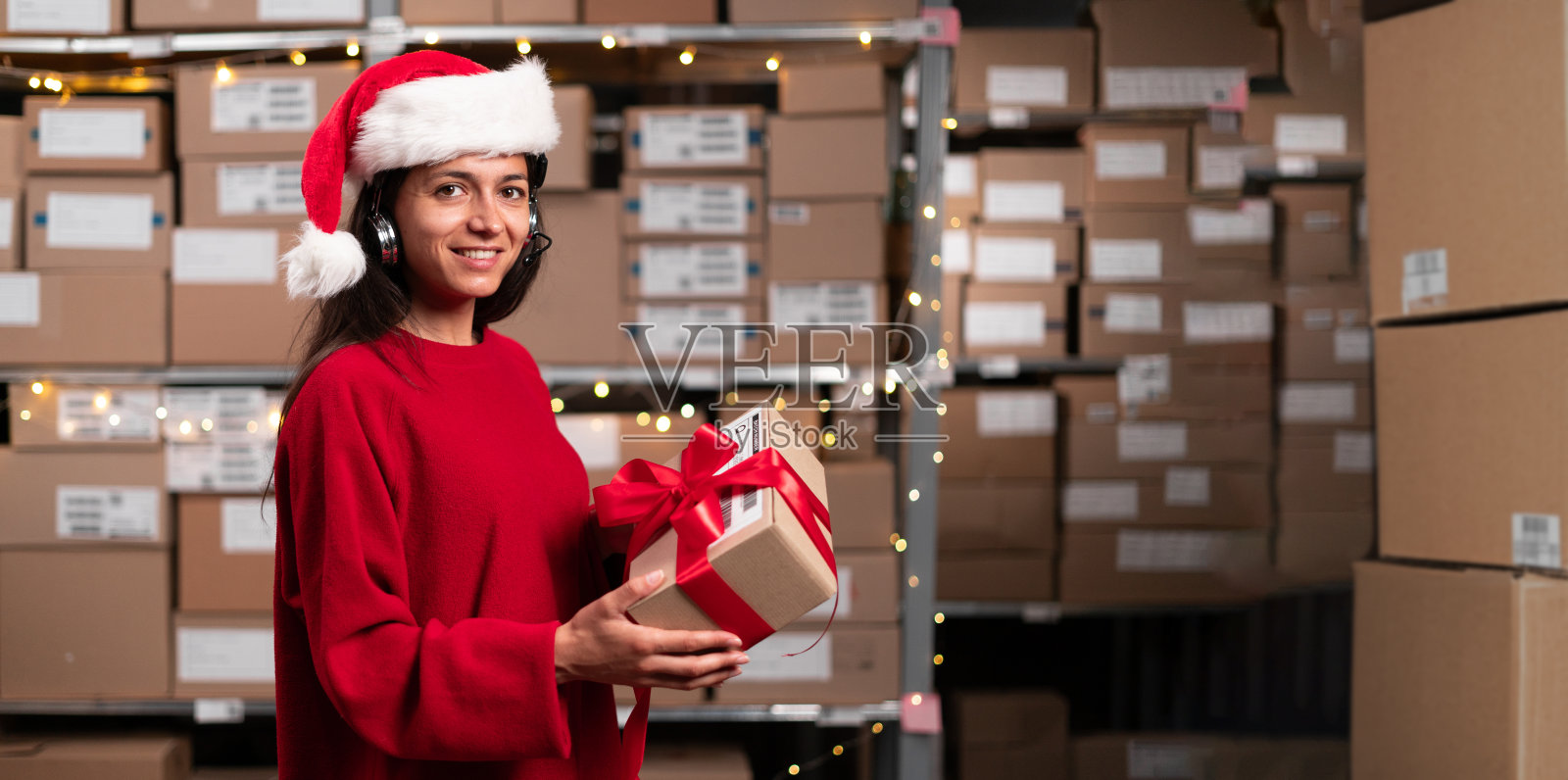 一位快递员戴着语音拾取耳机说话，手里拿着红丝带礼盒。照片摄影图片