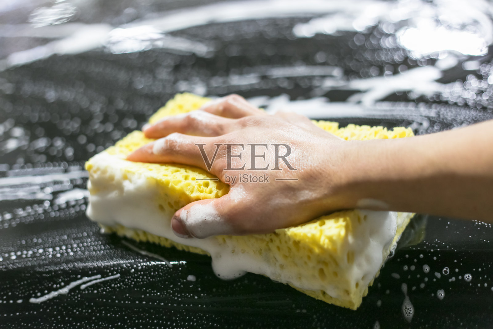 维修人员清洗黑色汽车的特写镜头。用泡沫和海绵洗车的过程。用黄色海绵洗车的男子。照片摄影图片