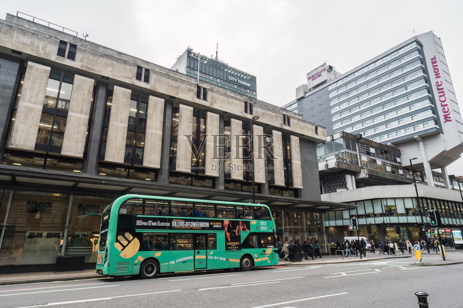 停在银行办公大楼外的绿色巴士，背景是行人照片摄影图片