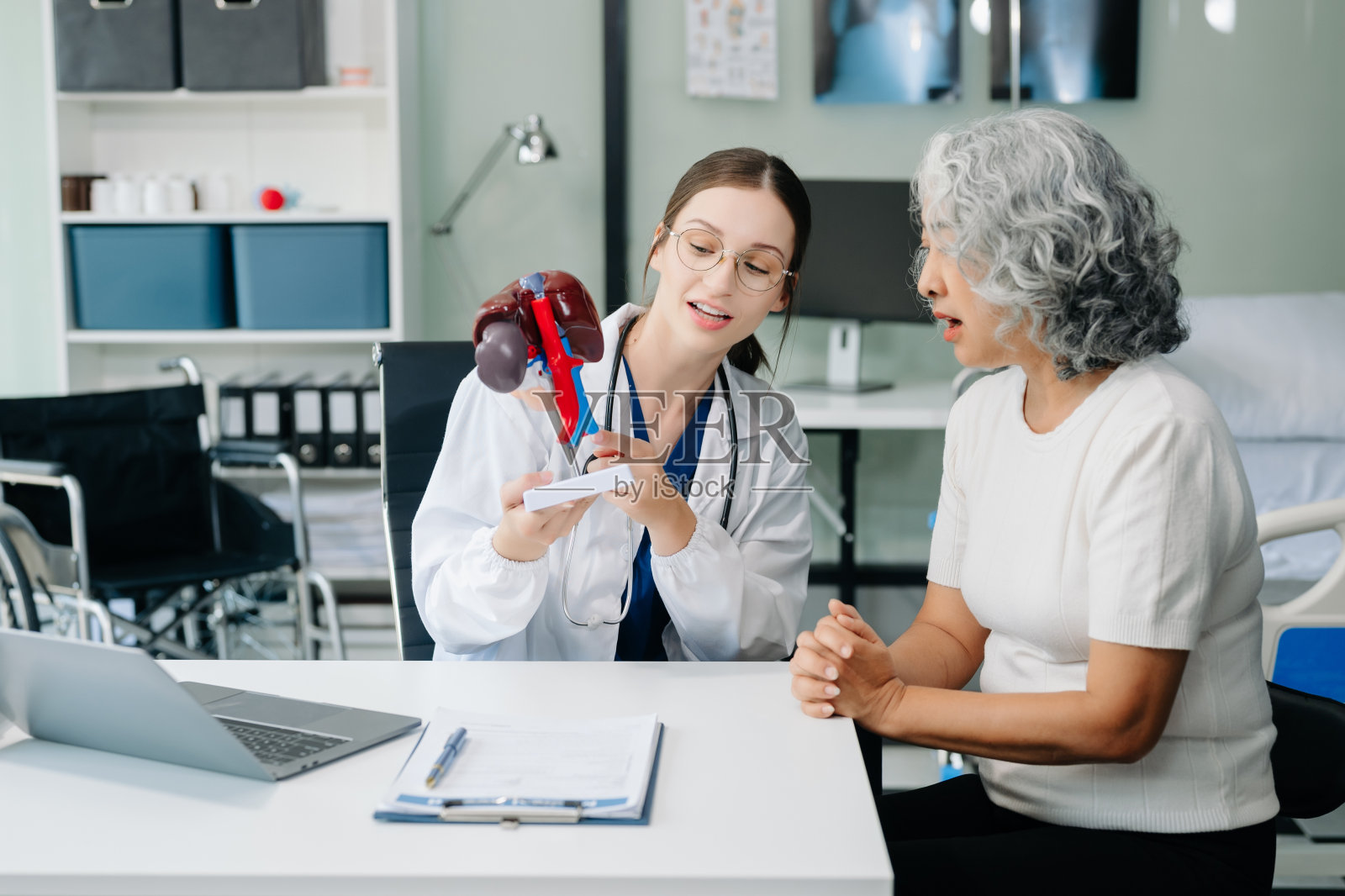 白衣医生一边讨论一边做笔记，一位亚洲老人躺在床上给病人注射生理盐水照片摄影图片