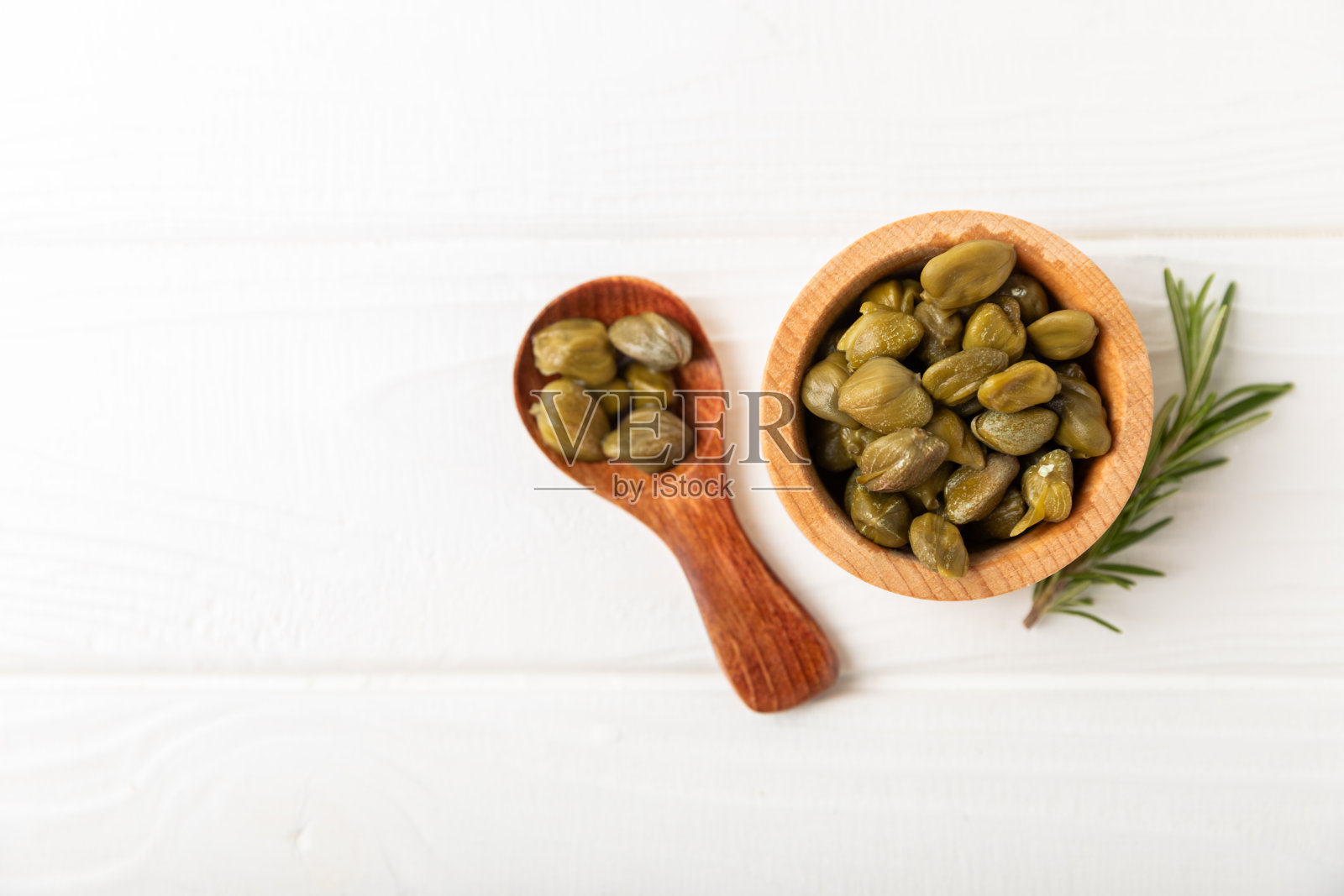 木桌上的玻璃罐子里装着刺山柑。刺山柑加海盐和迷迭香。腌酸豆。地中海菜的食材。有机香料和调味料。副本的空间。照片摄影图片