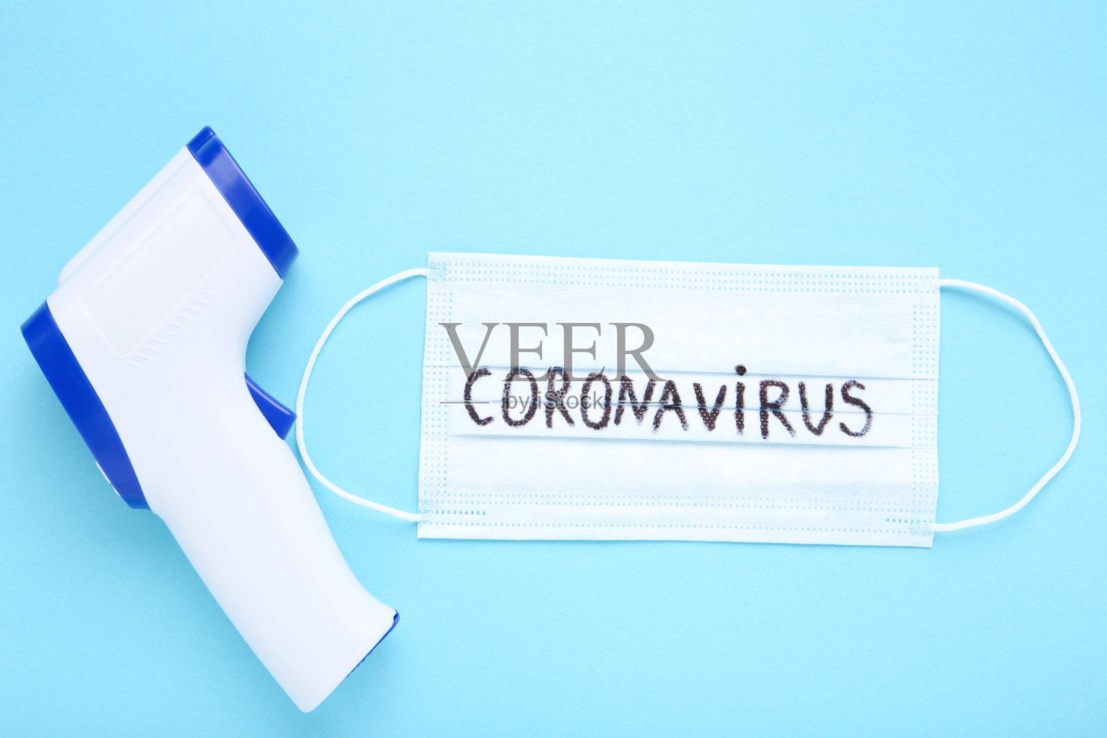 蓝色背景上印有冠状病毒和红外温度计的医用口罩照片摄影图片