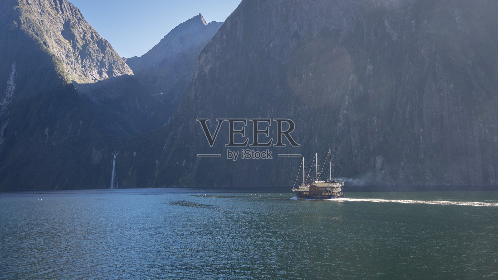 新西兰峡湾，小船穿过险峻的岩壁和远处的瀑布照片摄影图片