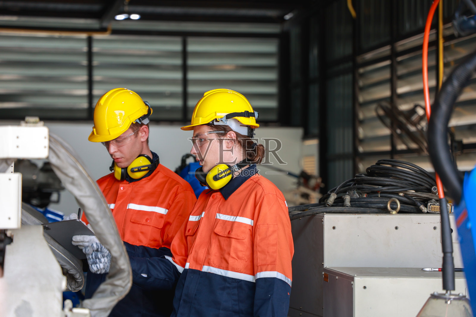 戴着安全帽的白人男性工程师在工业环境中操作和讨论机器人照片摄影图片