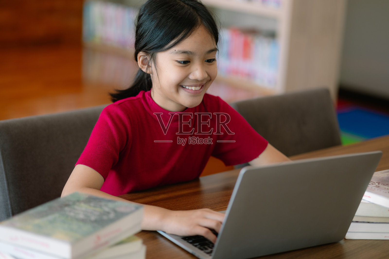 一个小女孩坐在桌子旁，桌上放着一台笔记本电脑和几本书照片摄影图片