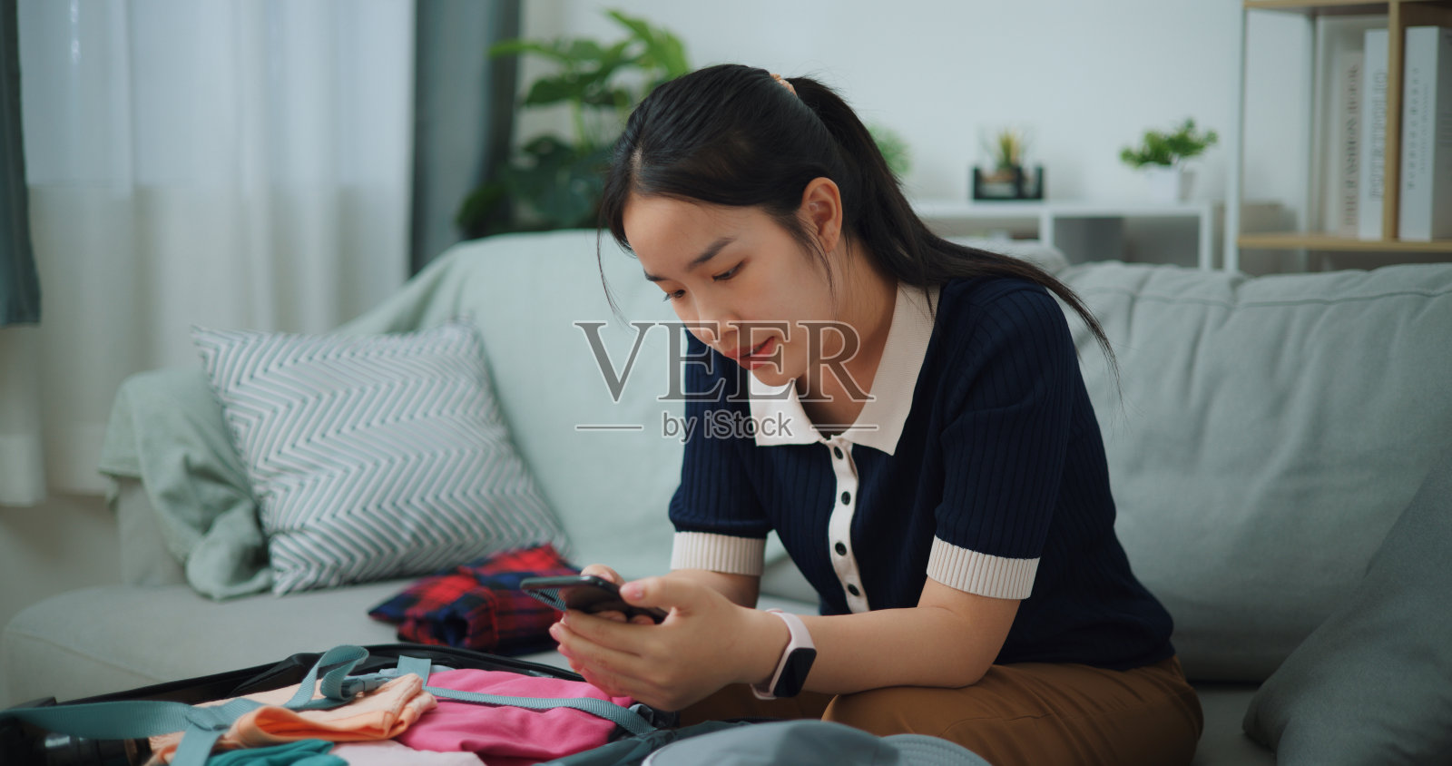 微笑的女人一边收拾行李一边用手机。照片摄影图片