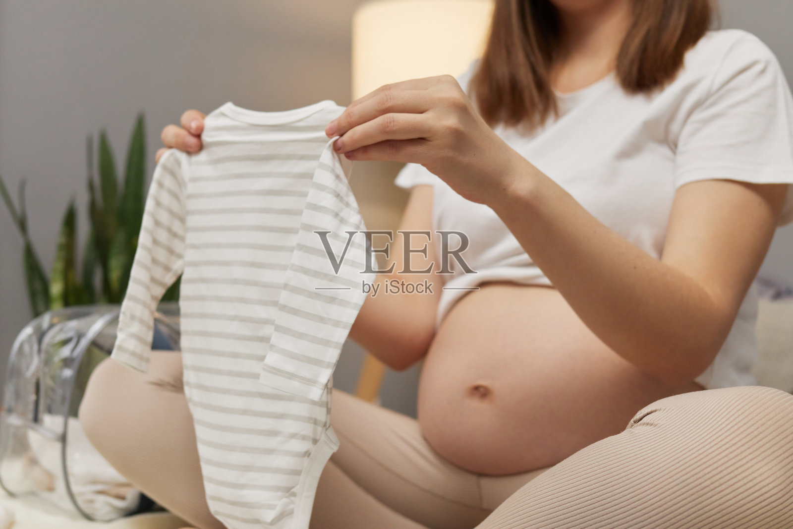 不知名的孕妇在家里为妇产医院准备婴儿服装，欣赏着为未来的小婴儿准备的条纹服装照片摄影图片