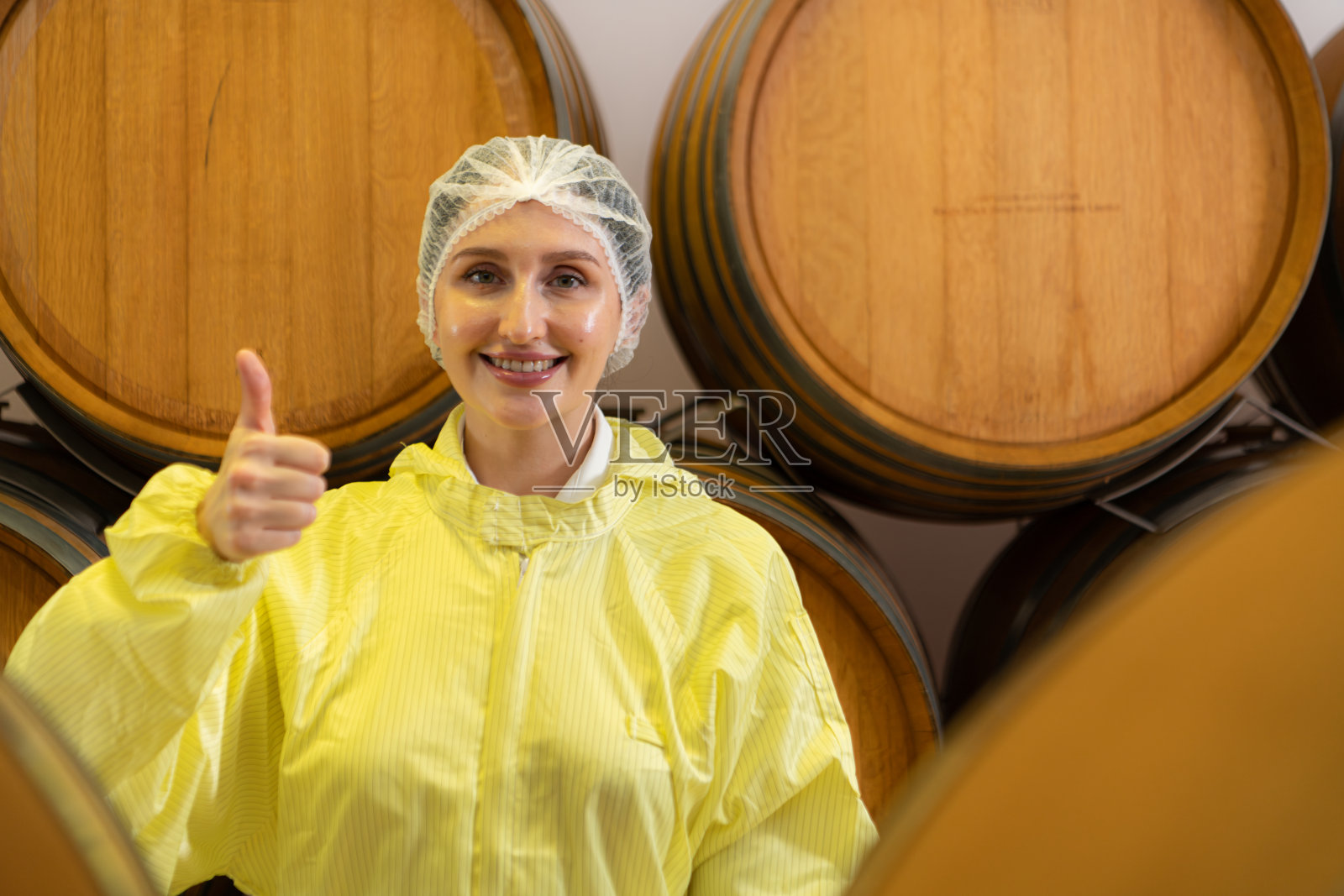 穿着黄色制服的女酿酒师站在酒窖里微笑着照片摄影图片