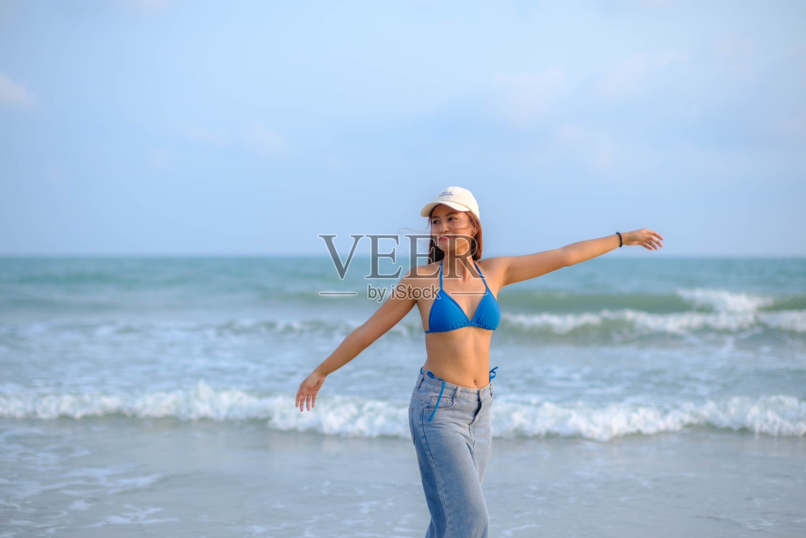 美丽的亚洲模特戴着帽子，穿着泳衣，在海滩上摆姿势。照片摄影图片