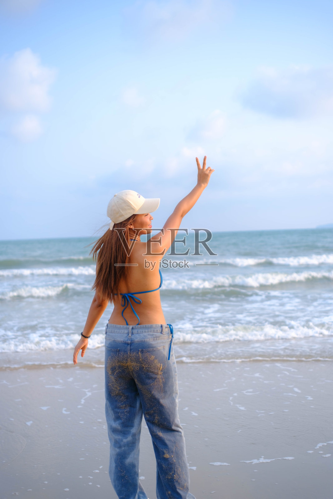 美丽的亚洲模特戴着帽子，穿着泳衣，在海滩上摆姿势。照片摄影图片